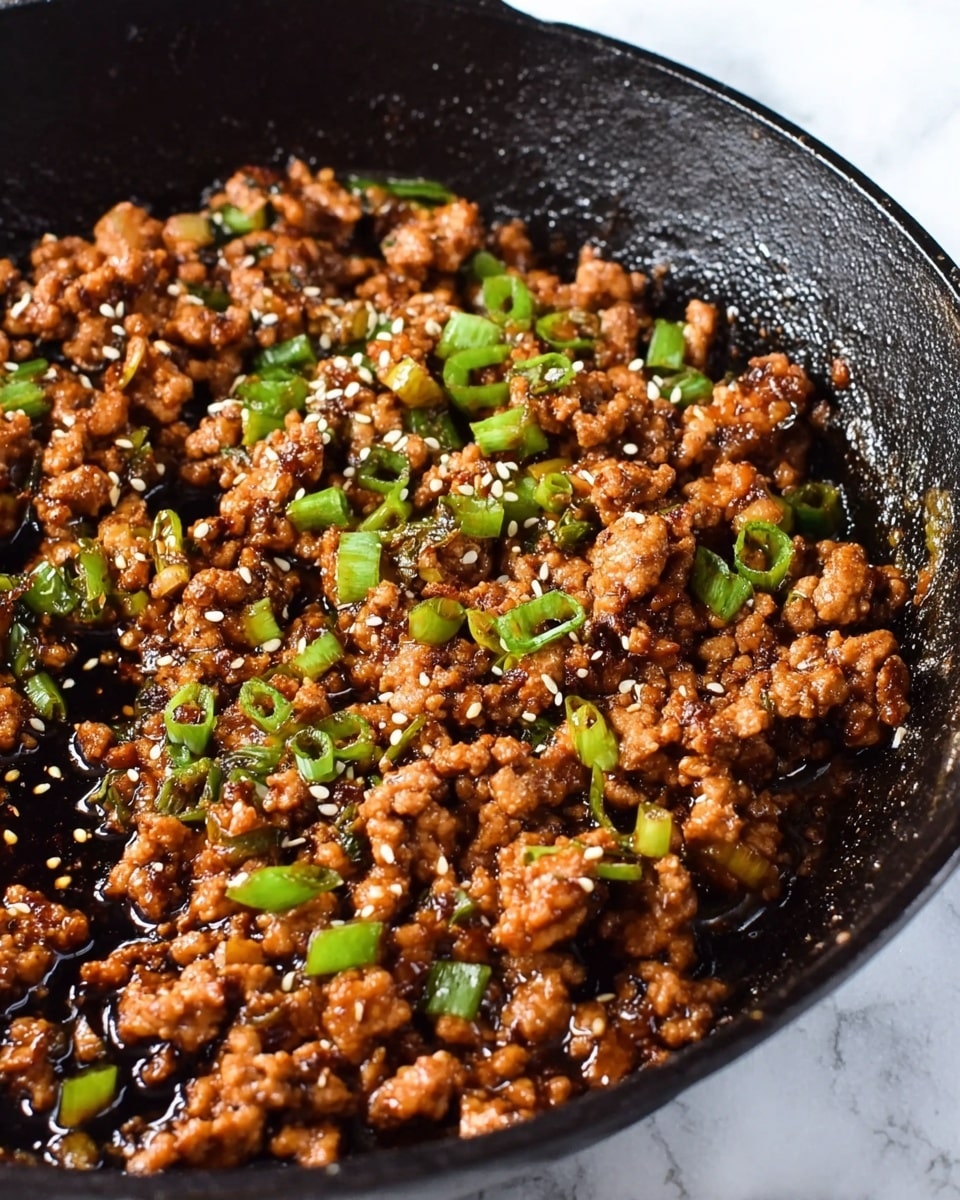 A close-up view of a black cast iron skillet filled with cooked ground meat that is brown and slightly crispy, mixed with small green pieces of chopped scallions scattered evenly on top. The dish is also sprinkled with white sesame seeds adding a light texture contrast. The meat looks moist and coated with a dark glossy sauce that pools slightly at the edges. The skillet is sitting on a white marbled surface. photo taken with an iphone --ar 4:5 --v 7