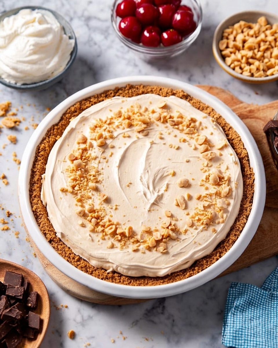 The image shows a dessert with three main layers in a white pie dish on a white marbled surface. The bottom layer is a light brown crumb crust forming a thick base and edges. On top of the crust is a thick layer of creamy, light beige filling with a smooth, slightly swirled texture. The top layer is sprinkled with small pieces of crushed peanuts spread evenly over the creamy filling. Surrounding the pie are bowls containing whole red cherries, whipped cream, chopped peanuts, and chocolate chunks on a wooden board. Photo taken with an iphone --ar 4:5 --v 7