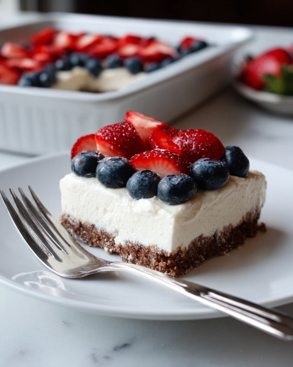 The image shows a square piece of dessert on a white plate with a silver fork beside it. The dessert has three layers: the bottom layer is brown and crumbly, the middle layer is thick, white, and creamy, and the top layer is decorated with fresh fruits. On the top, there are two rows of blueberries followed by a row of strawberries that are cut in half and placed neatly. In the background, there is a white baking dish with more of the same dessert. The surface is a white marbled texture. photo taken with an iphone --ar 4:5 --v 7