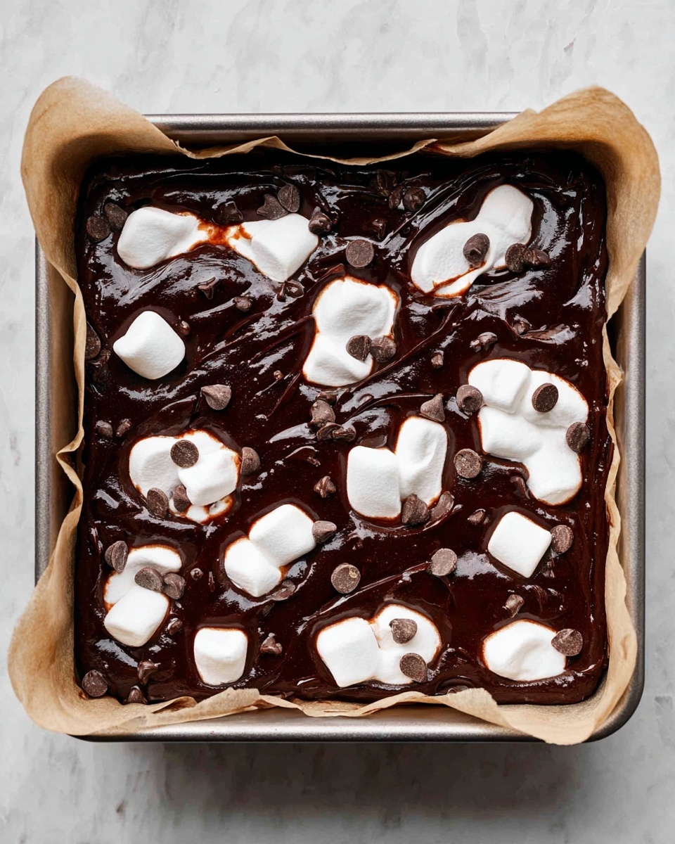 A square baking pan filled with a thick, dark brown chocolate batter base, unevenly spread across the pan. On top of the batter, patches of white marshmallow pieces are scattered, some partly melted with a slightly toasted brown tint on their edges. Small, darker chocolate chips are visible within the batter, peeking through the glossy chocolate surface. The pan is lined with parchment paper, and the whole scene is set on a white marbled surface. photo taken with an iphone --ar 4:5 --v 7