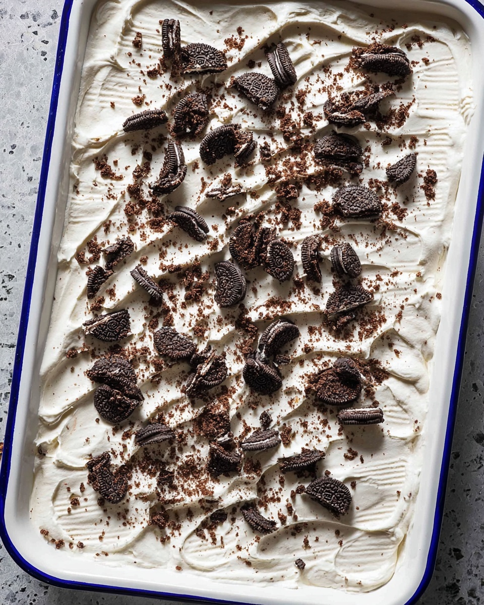 A single thick layer of smooth, white cream spread evenly in a white rectangular dish with blue edges, topped with many pieces of broken chocolate sandwich cookies scattered all over, showing a mix of dark brown cookie parts and white cream filling; the texture of the cream has soft ridges made by a spreading tool. Photo taken with an iphone --ar 4:5 --v 7