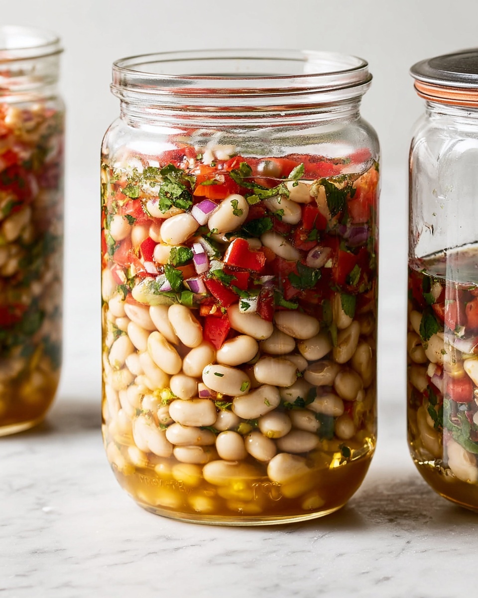The image shows a clear glass jar filled with a layered bean salad. The bottom layer is made of white beans soaked in a golden brown liquid, giving a shiny and slightly wet texture. Above this, the larger top layer is a mix of white beans, small bright red tomato pieces, chopped green herbs, and small bits of red onion, creating a colorful and fresh look. The jar is set on a surface with a white marbled texture, and a small part of another similar jar is visible on the right side. Photo taken with an iphone --ar 4:5 --v 7