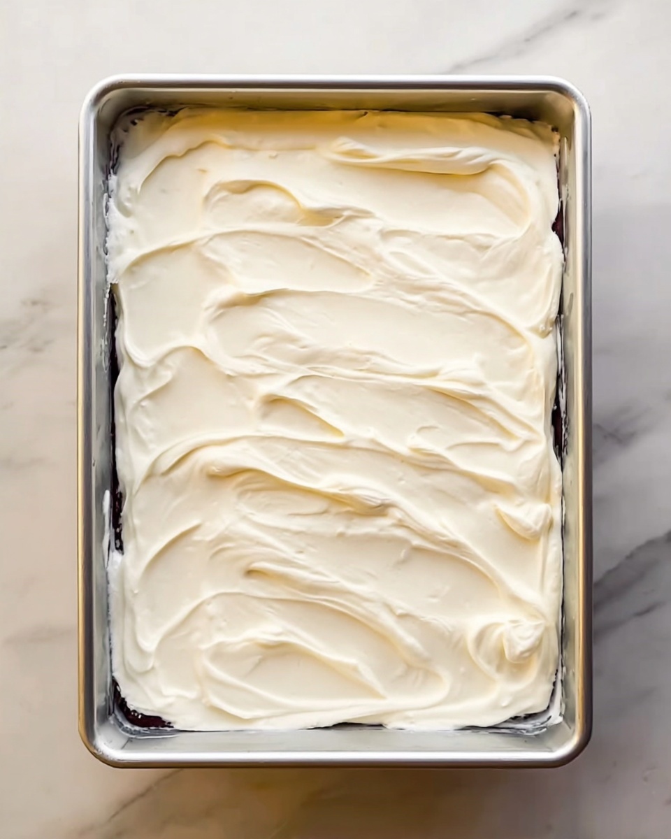 The image shows a rectangular metal pan filled with a dessert that has one thick layer of smooth, white cream spread evenly on top. The cream texture is soft with slight swirling patterns and gentle peaks, covering the entire surface inside the pan. The pan is placed on a white marbled surface. Photo taken with an iphone --ar 4:5 --v 7