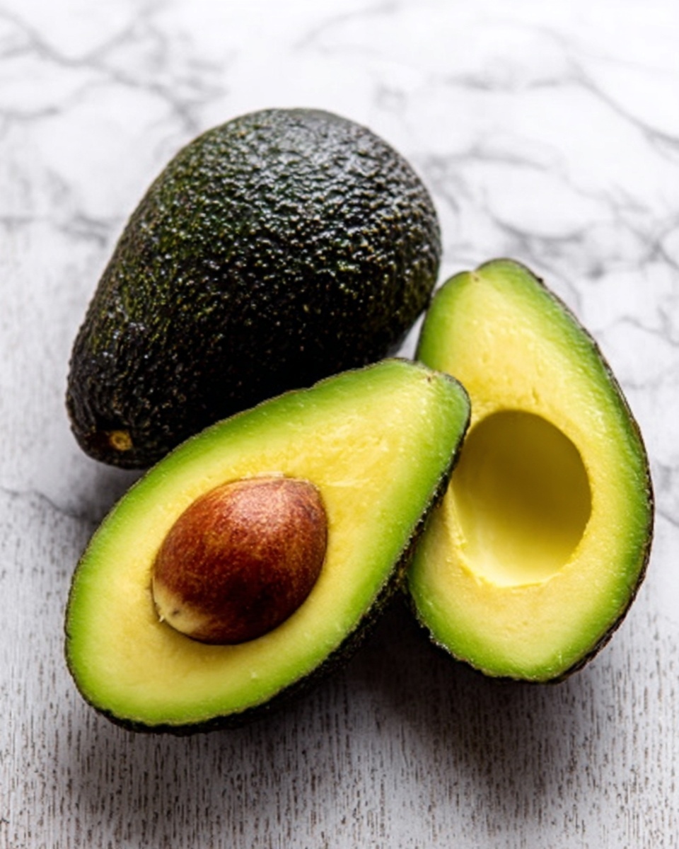 The image shows one whole avocado with dark green, bumpy skin resting next to two halves of an avocado on a white marbled surface. One avocado half has a large brown seed in the center with smooth light green flesh surrounding it, while the other half shows the hollow where the seed was, with the same smooth light green inside. The textures contrast between the rough outer skin and soft inner flesh, all arranged closely together. Photo taken with an iphone --ar 4:5 --v 7