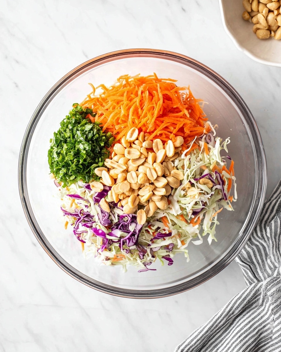 A clear glass bowl sits on a white marbled surface, filled with four distinct layers of ingredients. The bottom layer is a mix of shredded white and purple cabbage with thin carrot strips, showing a soft texture and mix of white, purple, and orange colors. On top of this, shredded bright orange carrots form the next layer, vibrant and fresh. To the side, there is a pile of chopped fresh green herbs, adding a rich green color and leafy texture. Piled on top in the center are pale brown peanuts with a smooth and firm texture. A white bowl is partially visible in the top right corner and a gray and white striped cloth is at the bottom right edge of the frame. Photo taken with an iphone --ar 4:5 --v 7