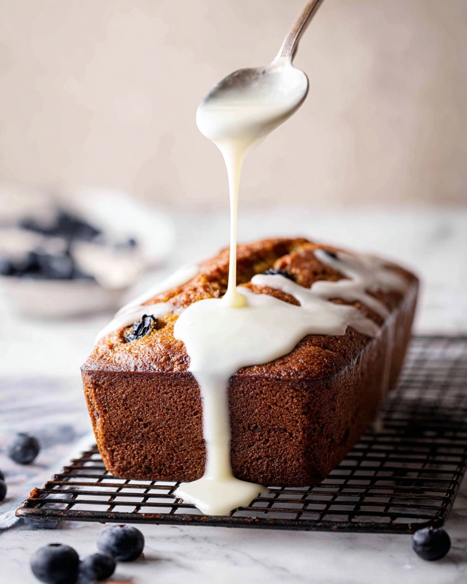 A rectangular loaf cake with a dark brown crust sits on a black wire rack placed on a white marbled surface; a thick white icing is being slowly poured from a spoon held above the cake, dripping down the sides and pooling slightly at the base, creating a glossy smooth layer on top; some blueberries are scattered loosely around the base of the rack, adding small bursts of dark blue color to the warm, rich tones of the cake and the bright white icing photo taken with an iphone --ar 4:5 --v 7