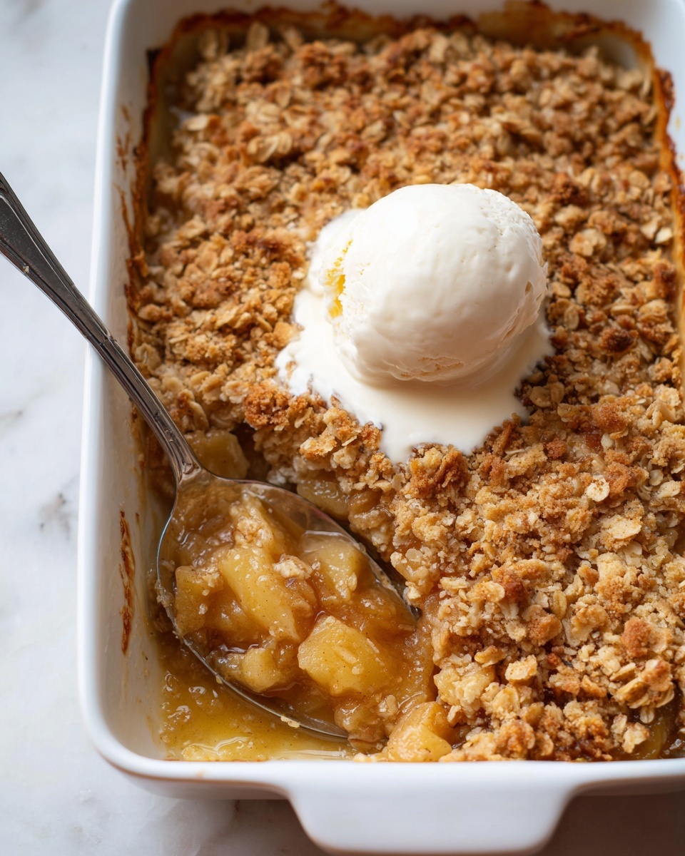 A white rectangular baking dish filled with a golden-brown apple crumble dessert, showing two layers: a bottom layer of soft, warm apple chunks in a shiny caramel-like sauce with a light golden color, and a thick top layer of crumbly oat topping that is textured and uneven in a mix of light brown and toasted oat colors. On top, there is a smooth, round scoop of white vanilla ice cream, slightly melting and blending into the crumble around it. A metal spoon is placed inside the dish on the left side, scooping out some of the apple filling. The dish rests on a white marbled surface. Photo taken with an iphone --ar 4:5 --v 7
