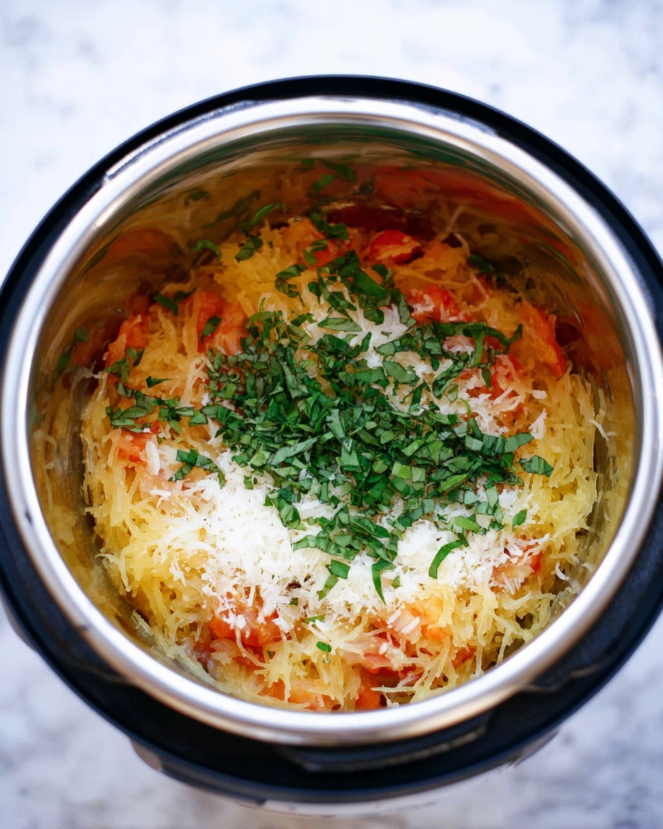Inside a shiny stainless steel pot, there are multiple layers of food. The bottom layer is light yellow spaghetti squash strands mixed with bits of soft orange tomato pieces. On top of that is a layer of finely grated white cheese. The highest layer is fresh green chopped basil leaves scattered evenly. The pot is surrounded by a black outer ring, and the scene is set on a white marbled surface. photo taken with an iphone --ar 4:5 --v 7
