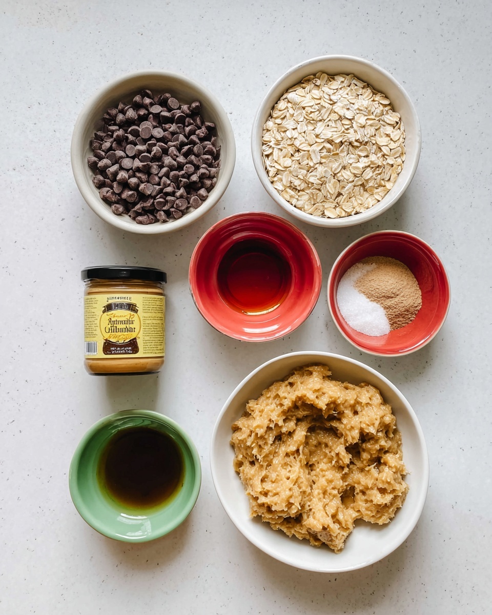 A top-down view of various baking ingredients arranged on a white marbled surface. In the middle right, a white bowl is filled with light brown mashed banana with a chunky texture. To the left of it, a white bowl holds small dark brown chocolate chips. Above this, there is a white bowl full of light beige rolled oats with visible flakes. At the top right, a small white bowl with a red interior contains light brown and white powders. At the top left, a small red bowl with a shiny smooth interior holds a dark amber liquid. Below the oats, a small green bowl contains a similar dark amber liquid. On the far left is a small jar of smooth almond butter with a yellow and black label. Everything is placed neatly on the clean white marbled surface. Photo taken with an iphone --ar 4:5 --v 7