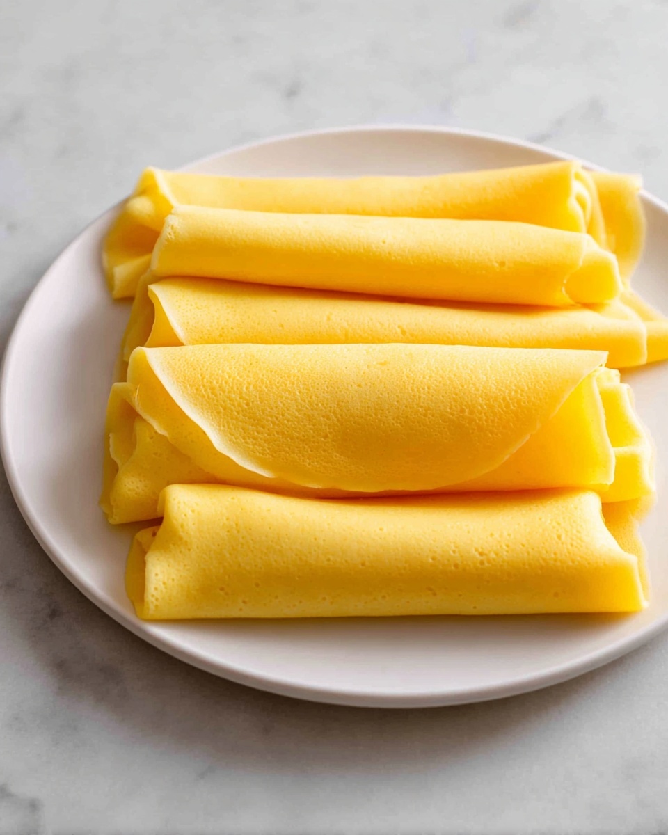 The image shows a white plate with six neatly folded yellow crepes stacked in two rows. Each crepe is smooth and soft with a slight shine, folded into a rectangular shape with clean edges, stacked tightly and lying flat side by side. The plate sits on a white marbled surface, and the crepes' bright yellow color contrasts with the clean white plate and background making them stand out clearly. photo taken with an iphone --ar 4:5 --v 7