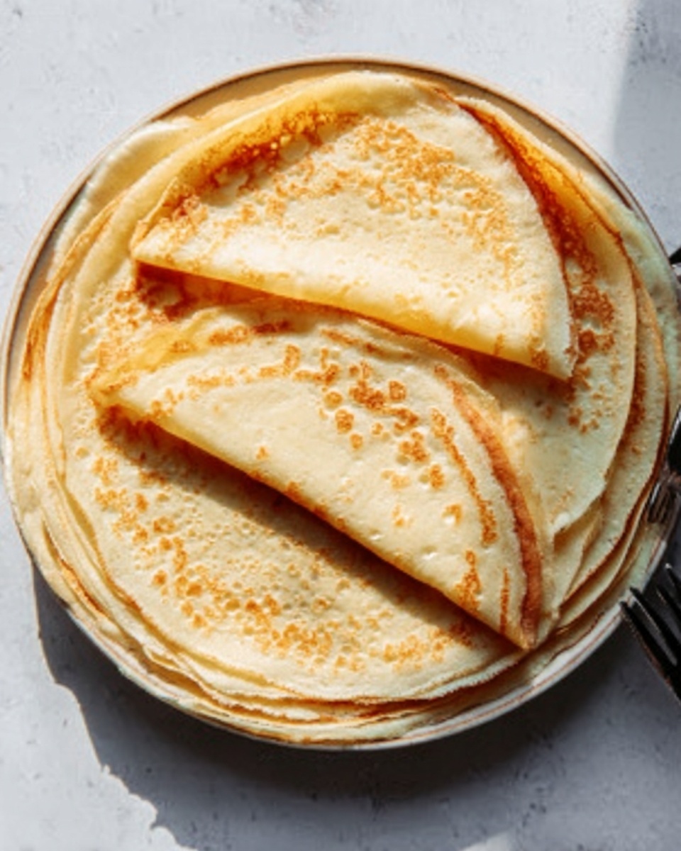 The image shows a stack of four thin crepes neatly folded in half and then folded again into quarters, arranged in a fan shape on a round white plate. The crepes have a light golden-yellow color with some soft brown spots, and their texture looks soft and slightly bubbly. The plate sits on a white marbled surface, and a woman's hand is visible next to the plate holding a fork with some food on it. The overall lighting is natural and bright. photo taken with an iphone --ar 4:5 --v 7