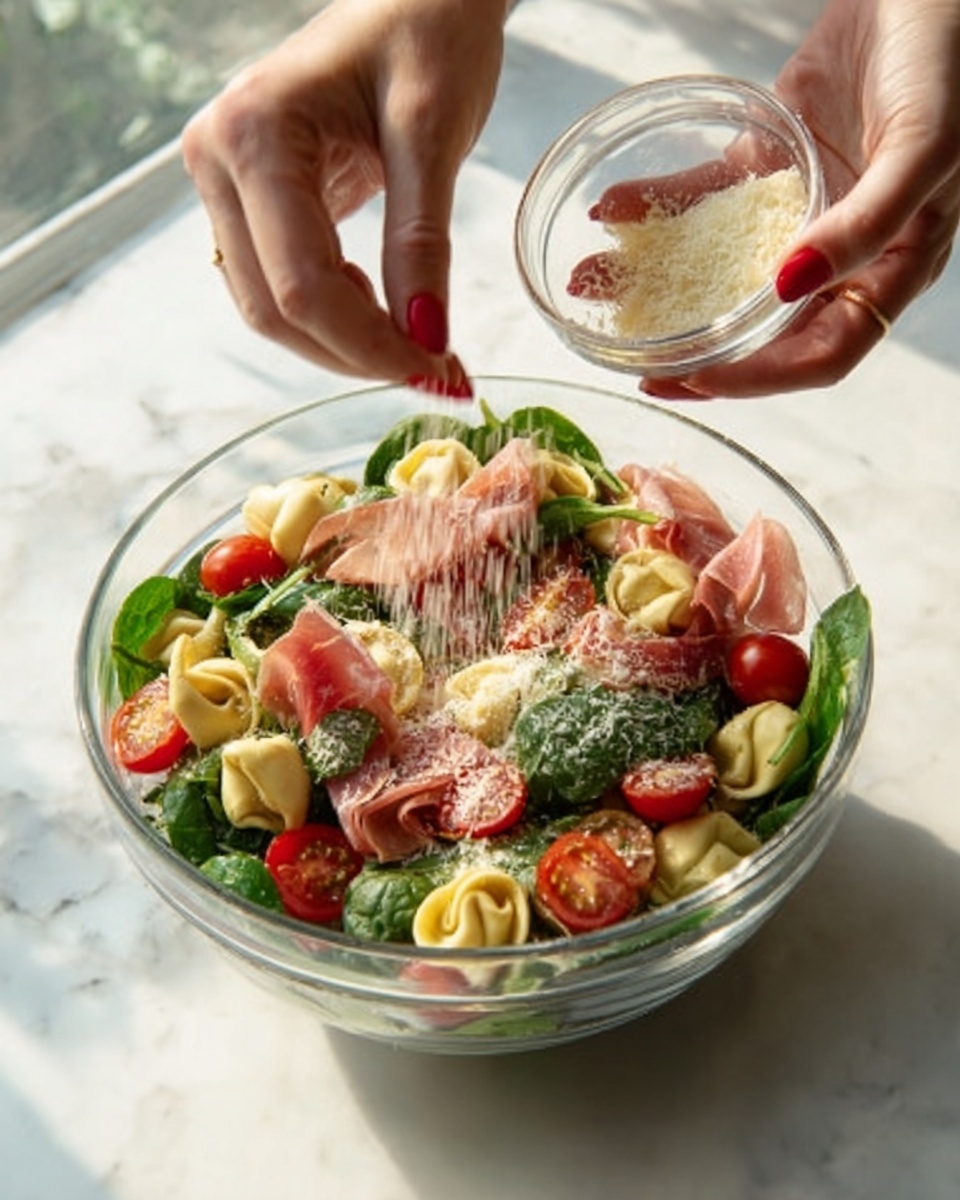 A clear glass bowl sits on a white marbled surface, filled with a fresh salad made of green spinach leaves, bright red cherry tomatoes, and pale yellow tortellini. Thin slices of pink prosciutto are layered between the greens, adding a soft, delicate texture. A woman's hand with red painted nails is sprinkling light grated cheese over the salad, held in a small clear bowl in the other woman's hand. Bright natural light highlights the fresh ingredients, creating a vibrant and appetizing look. photo taken with an iphone --ar 4:5 --v 7
