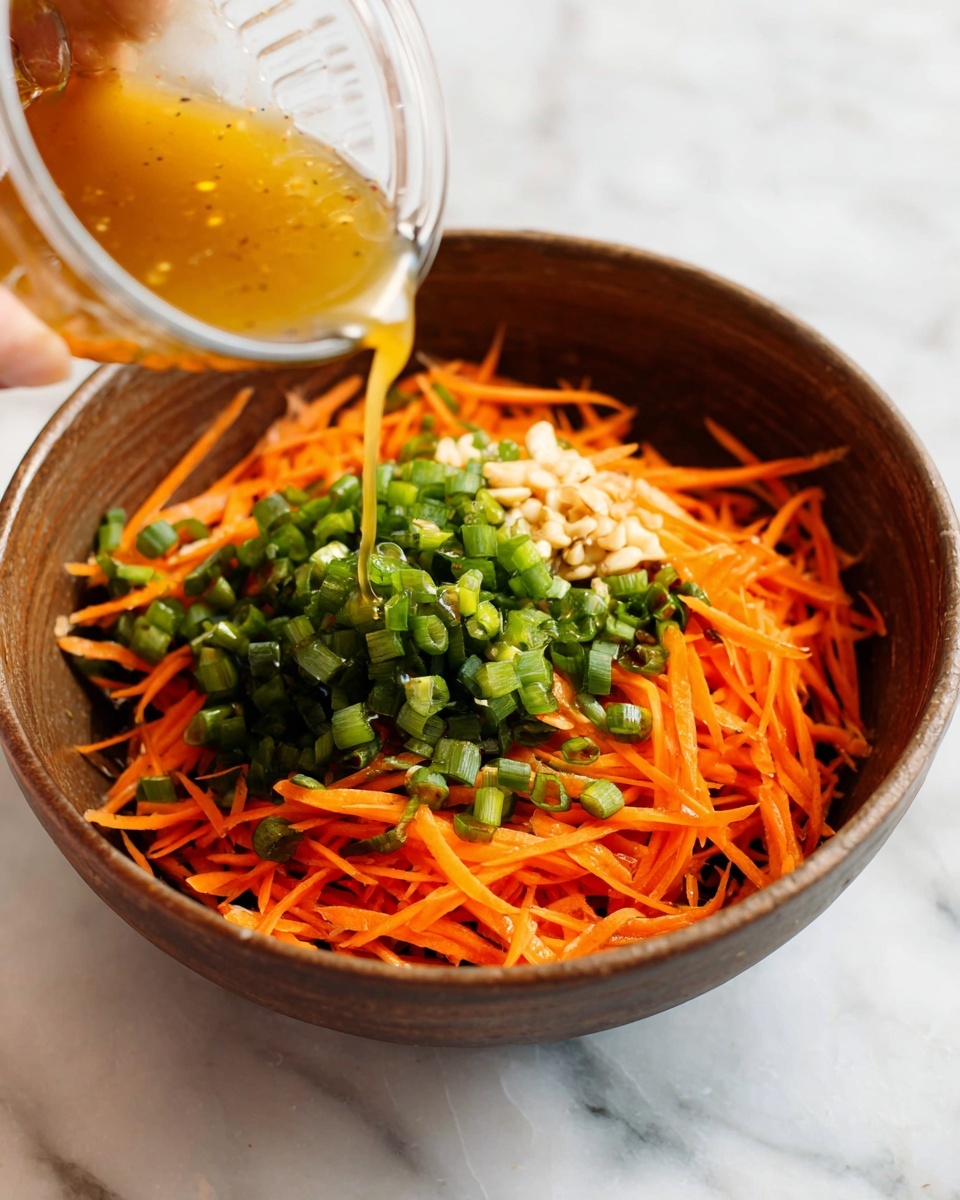 In a brown bowl sitting on a white marbled surface, there are three visible layers: the bottom layer is thin orange carrot strips spread evenly across the bowl, the middle layer is chopped green onions placed in the center, and the top layer is a light brown dressing being poured from a clear container, creating a glossy texture over the green onions and carrots; a woman's hand is holding the container, pouring the dressing. photo taken with an iphone --ar 4:5 --v 7