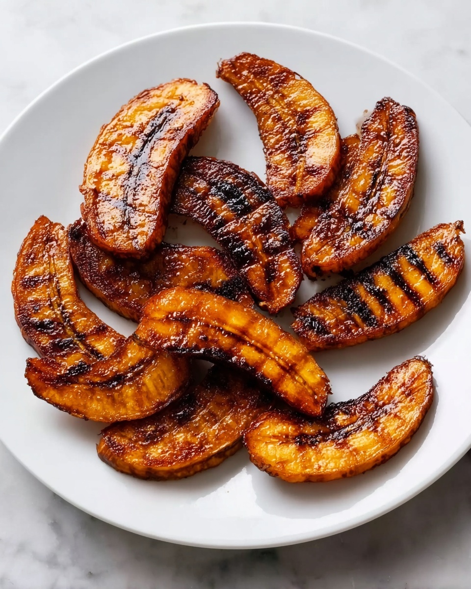 The image shows a white plate holding nine pieces of grilled, caramelized plantains arranged casually. Each plantain slice is golden brown with dark brown char marks creating a striped pattern, giving a slightly shiny look. The plate sits on a white marbled surface, adding a clean and simple background to the rich colors of the plantains. The lighting highlights the glossy texture and the crisp edges of the grilled plantains, making them look warm and inviting. photo taken with an iphone --ar 4:5 --v 7