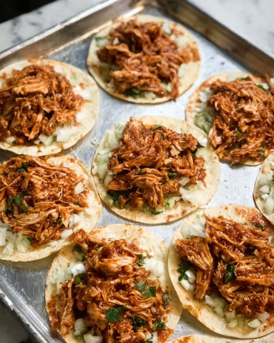 The image shows multiple small white plates each holding a single small round tortilla. On each tortilla, there is a layer of chopped white onions spread evenly, topped with a thick layer of shredded brown cooked meat mixed with some green herbs. The plates are arranged on a silver metal tray which rests on a white marbled surface. The scene looks natural and evenly lit, with no extra garnishes or decorations, focused on the simple, hearty tortillas with filling photo taken with an iphone --ar 4:5 --v 7