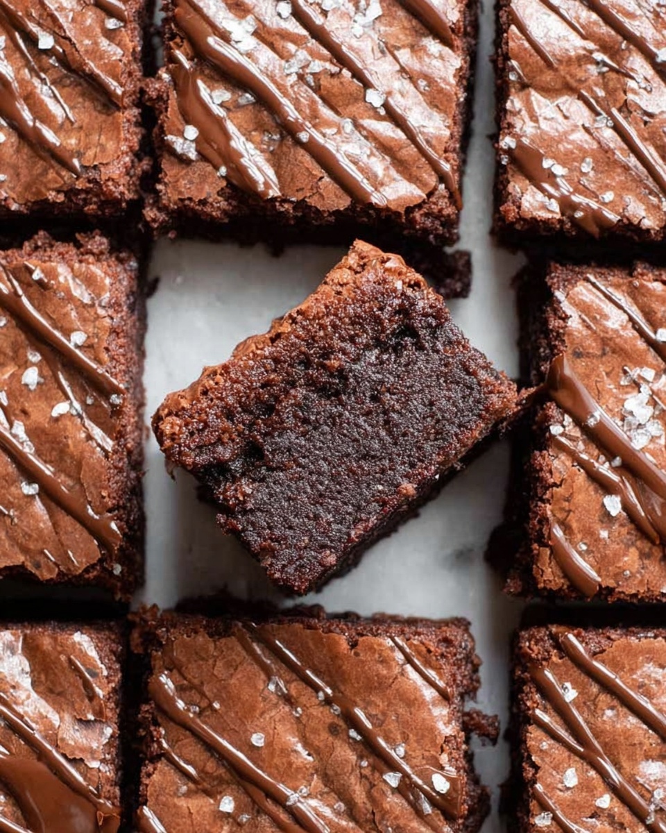 The image shows several square brownies arranged on a white marbled surface. Each brownie has two visible layers: the main dense, dark brown base with a cracked top layer, and a glossy milk chocolate drizzle spread unevenly across the top. Some brownies have small pieces of coarse sea salt sprinkled on top, adding texture. The brownies are close to each other but not touching, creating small gaps where crumbs and bits of chocolate are scattered. The lighting highlights the rich, moist texture and the contrast between the dark brownie and lighter chocolate drizzle. photo taken with an iphone --ar 4:5 --v 7