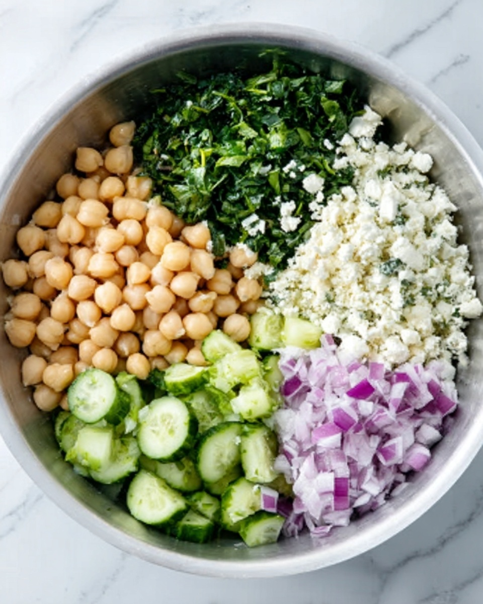 A white bowl filled with five separated sections of ingredients arranged in a circle on a white marbled surface. One section has a heap of light beige chickpeas with a smooth texture. Next to it, there is finely chopped dark green spinach. Adjacent to the spinach, there is a pile of small, white crumbled cheese. Beside the cheese, there are sliced green cucumber pieces with a shiny surface. The last section contains finely chopped purple onions. The overall look is fresh and colorful with a clear separation between each ingredient. Photo taken with an iphone --ar 4:5 --v 7