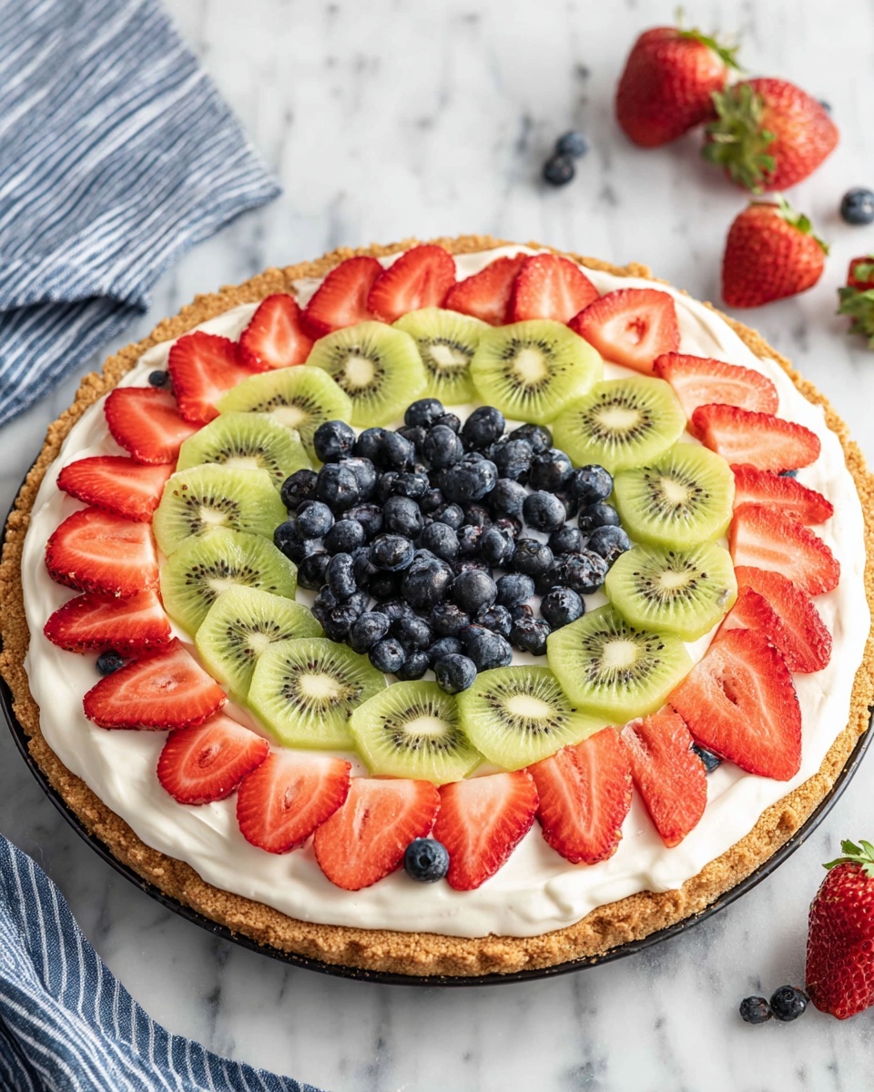 A round dessert with three clear layers is shown from above. The bottom layer is a light brown, thick cookie crust with a rough texture spread evenly in a white plate. The middle layer is smooth, white cream, evenly spread on top of the crust. The top layer is made of fresh fruit arranged in a circular pattern, starting from the outer edge with sliced red strawberries, followed by green kiwi slices with black seeds, then more strawberries, and blueberries placed both alone and grouped in the center forming a small mound. The dessert is placed on a white marbled surface with a blue and white striped cloth and some whole strawberries at the top left. Photo taken with an iphone --ar 4:5 --v 7