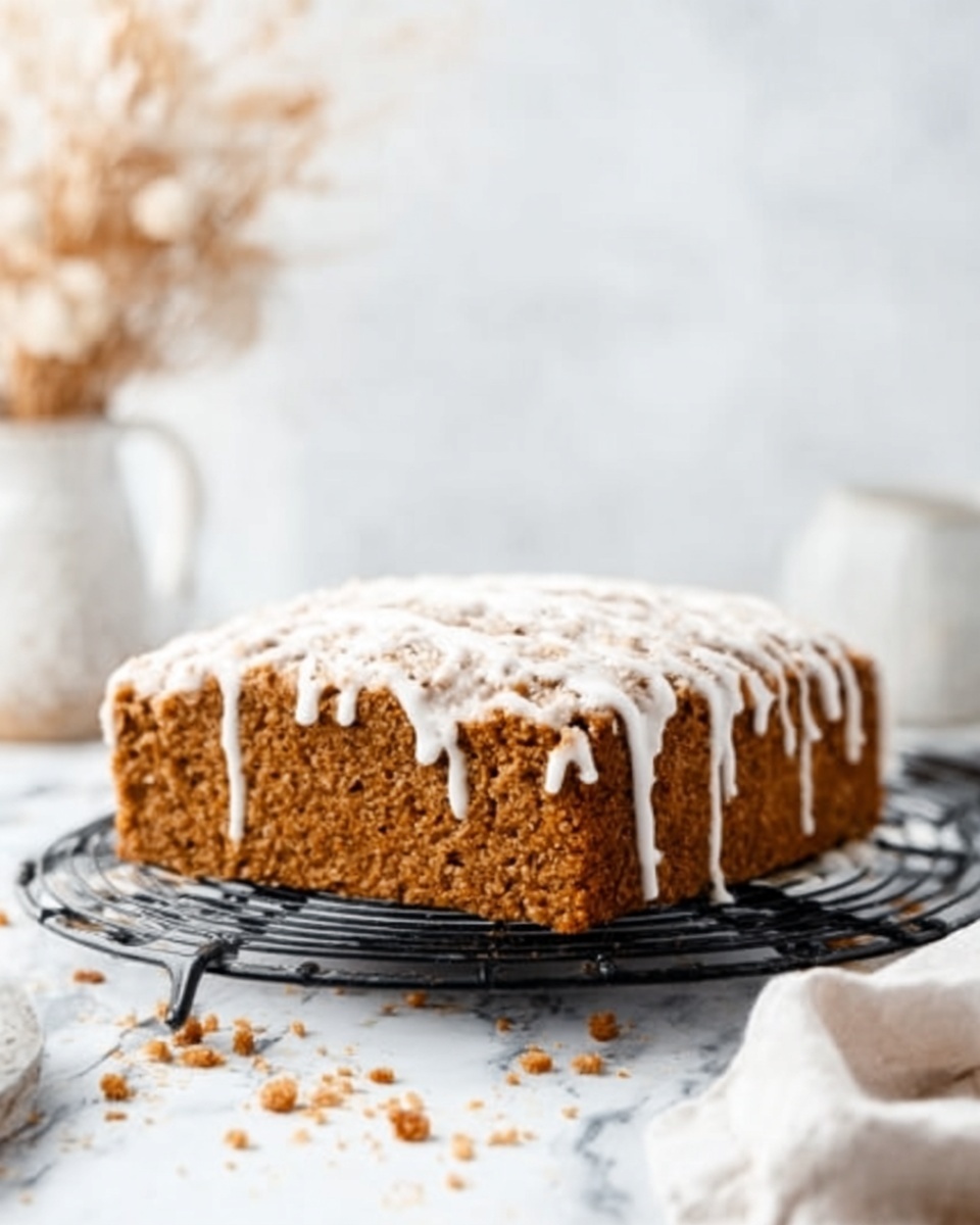 There are nine square pieces of a soft cake with a crumbly, dark brown streusel layer on top that is drizzled with white icing. The cake itself is a warm orange-brown color, showing a moist texture. The pieces are arranged on white parchment paper over a black cooling rack, all placed against a white marbled surface. The cake squares vary slightly in size, with one piece turned on its side, clearly showing two layers: a thick orange-brown bottom layer and the dark crumbly top streusel layer with icing. Photo taken with an iphone --ar 4:5 --v 7