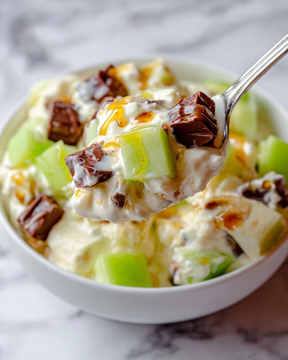 The image shows a close-up of a creamy dessert in a white bowl on a white marbled surface. The dish has three main layers visible within each spoonful: small cubes of green apple with smooth, shiny skin; soft white cream mixed throughout; and scattered dark brown pieces that look like chocolate or candy. There are also light drizzles of golden syrup on top, adding a glossy shine. The spoon lifts a mix of these layers, showing the dessert’s thick and creamy texture with bright and rich colors contrasting well. Photo taken with an iphone --ar 4:5 --v 7