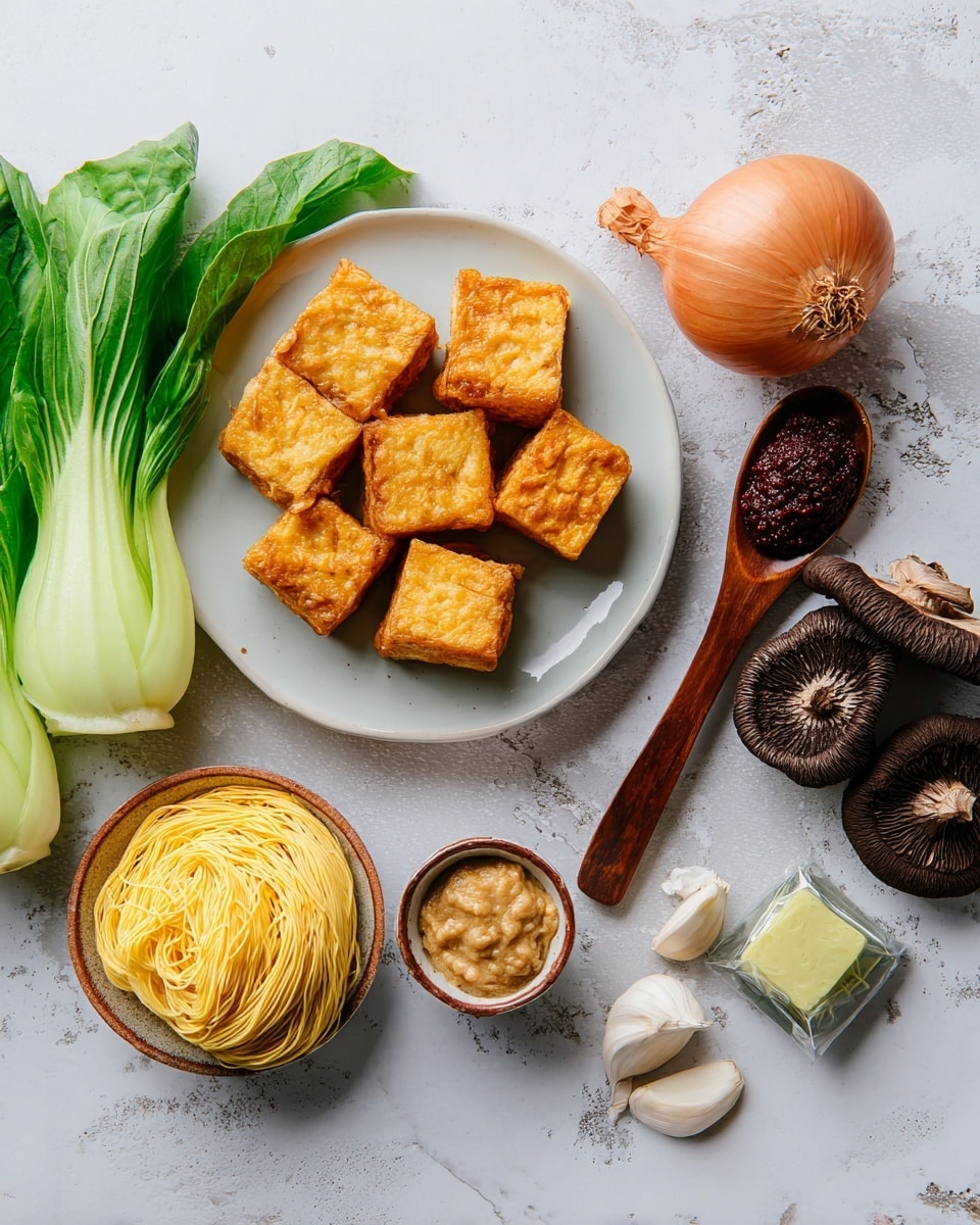 The image shows a white plate filled with six golden-brown fried tofu cubes arranged closely on the left side. To the right of the plate, a dark wooden spoon holds a dollop of dark red paste. Beside the spoon, there is a whole brown shallot with its dry outer skin still intact. Below the shallot, a small nest of dry yellow noodles rests directly on the white marbled surface. Near the bottom middle right, there is a small brown bowl filled with a light brown paste. Below the bowl, there is a greenish-yellow seasoning cube partially unwrapped in clear plastic. To the bottom left, fresh bright green bok choy leaves extend into the scene, with a peeled clove of garlic and a piece of ginger root placed near the greens. At the bottom right, a few dark brown shiitake mushrooms sit in a small white ceramic bowl with a brown rim. The whole composition is laid out on a white marbled texture background photo taken with an iphone --ar 4:5 --v 7
