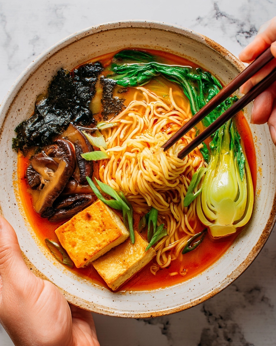A bowl with rich orange-red broth fills the base, topped with light yellow noodles piled in the center, lifted slightly by dark wooden chopsticks. To one side, bright green bok choy with shiny leaves rests partly in the soup. Near the back, dark brown mushrooms and a large, wrinkled black seaweed sheet lean against the bowl edge. Pieces of light brown tofu float near the broth's surface, and some green onion slices add extra color on top. The bowl sits on a white marbled surface. photo taken with an iphone --ar 4:5 --v 7
