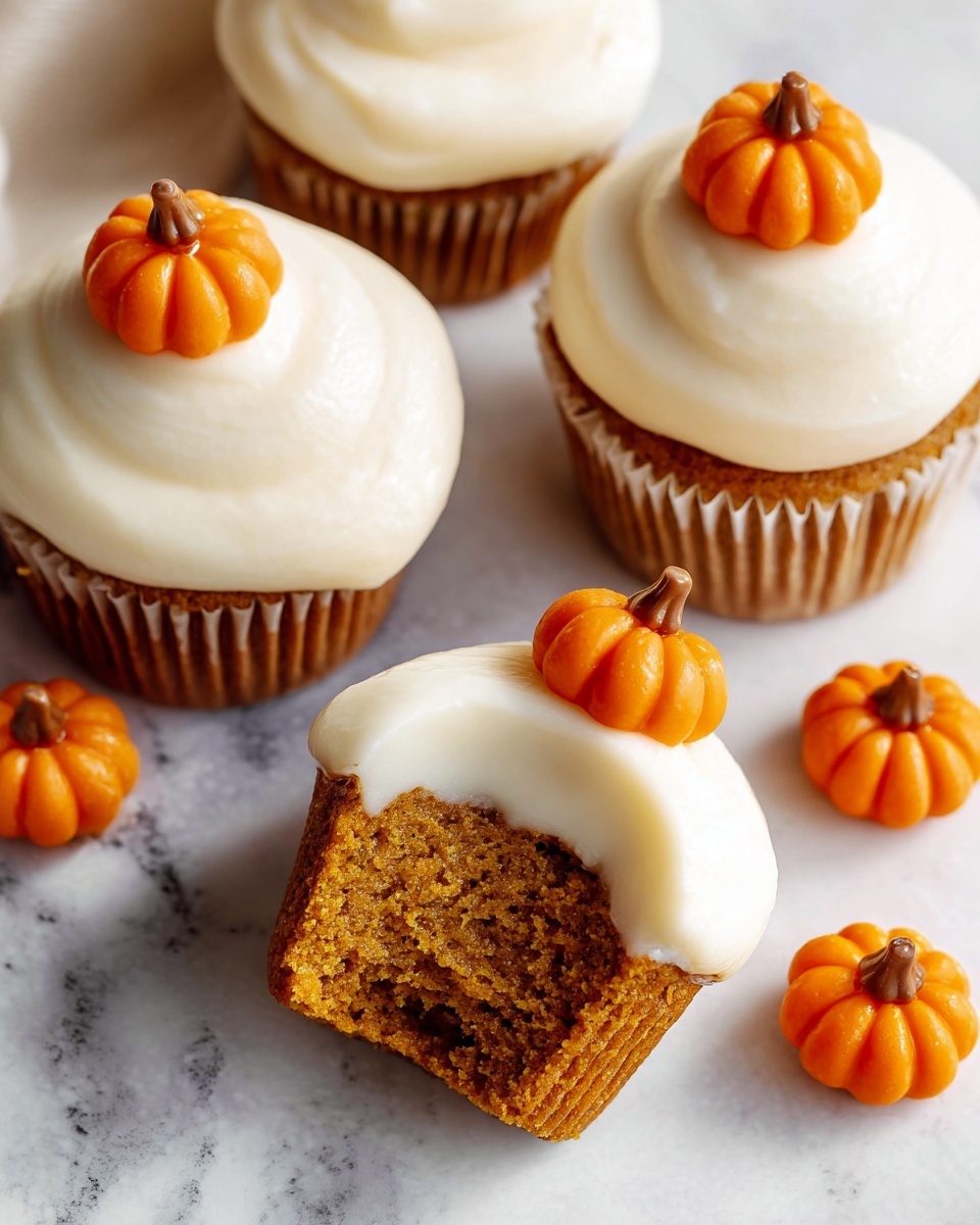 The image shows five pumpkin cupcakes on a surface with white marbled texture. Each cupcake has two layers: the bottom layer is soft, moist, orange-brown cake, and the top layer is smooth, thick white cream frosting swirled in a rounded shape. Four whole small orange pumpkin decorations with brown stems are placed on top of four cupcakes, and one cupcake is missing a bite, showing the inside texture of the cake. The cupcakes are arranged casually with some loose pumpkin decorations near them. Photo taken with an iphone --ar 4:5 --v 7