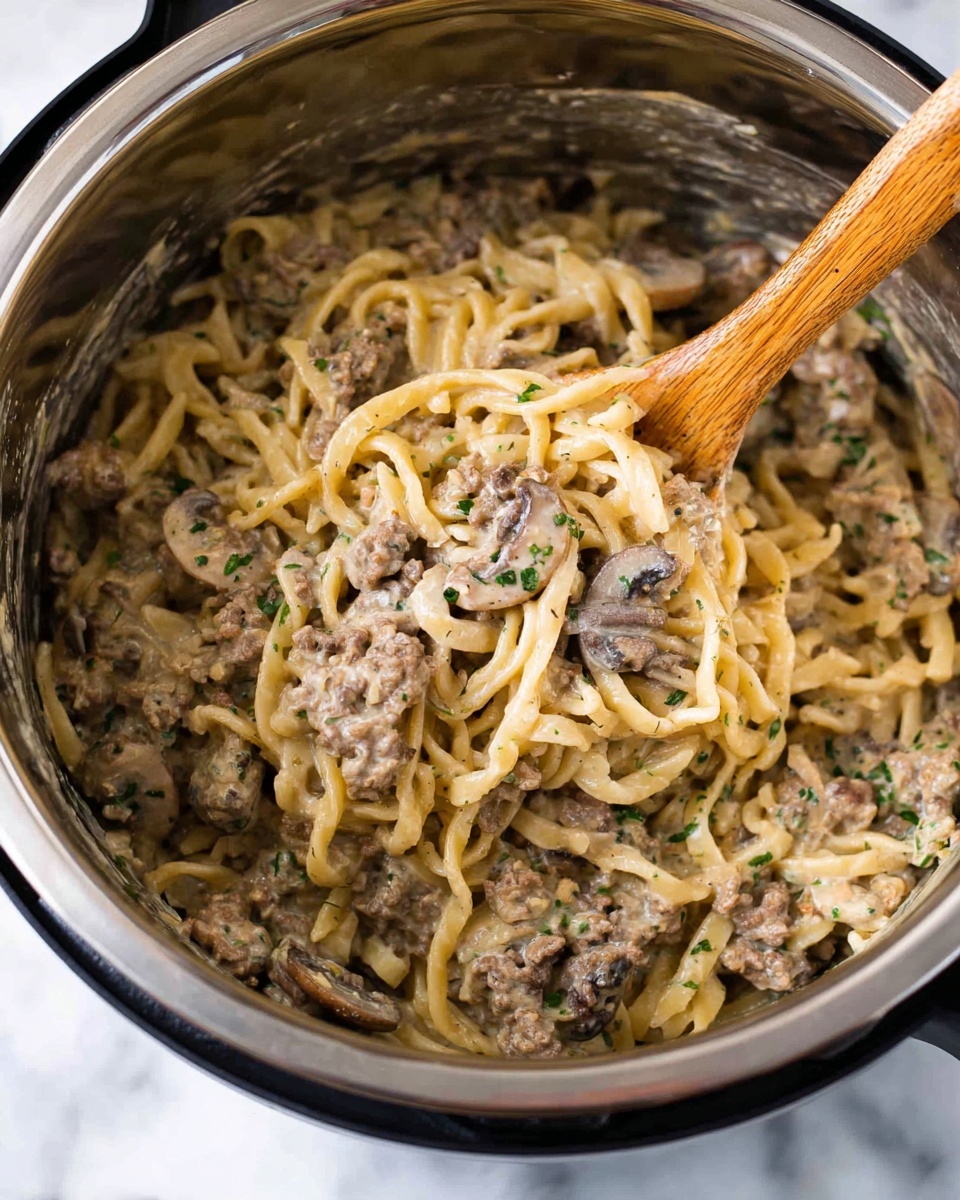 The image shows a stainless steel pot filled with creamy pasta mixed with small pieces of cooked meat and mushrooms. The pasta has a light beige color, and the meat pieces are brown, blending into the sauce, which gives a smooth and slightly thick texture throughout the dish. Green herbs are lightly sprinkled on top, adding a touch of color. A wooden spoon is partially submerged in the pasta, lifting some of it. The background is a white marbled surface. Photo taken with an iphone --ar 4:5 --v 7