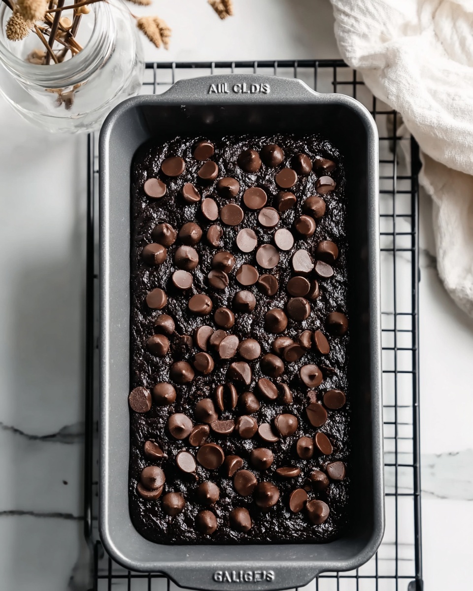 A close-up view of a dark chocolate brownie dough filled in a single rectangular baking pan with a textured matte grey finish labeled
