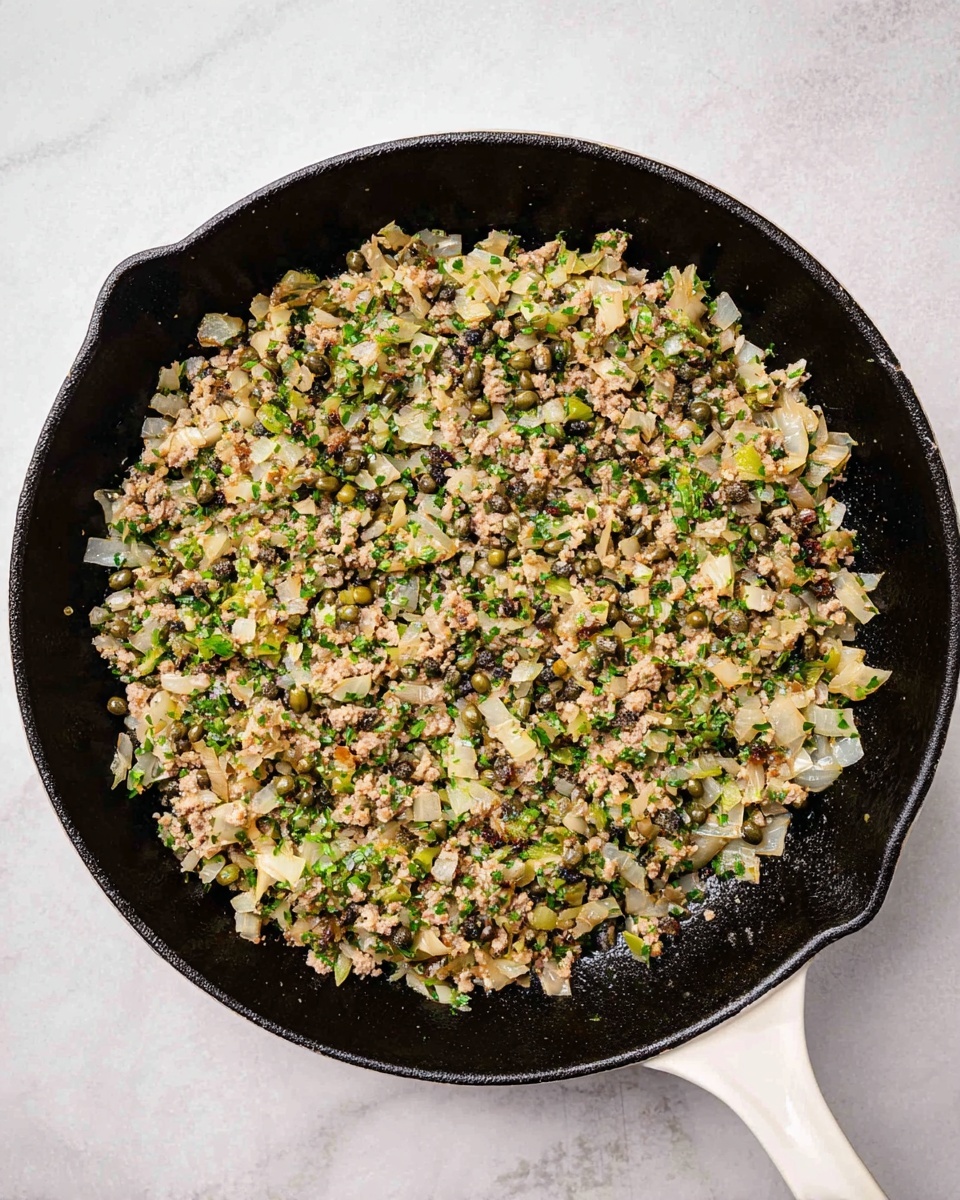 A white cast iron pan holds a single layer of cooked chopped onions mixed with small bits of light brown meat, green herbs, and capers, all evenly spread across the pan's dark black cooking surface. The onions appear translucent with a soft texture, while the green herbs add small colorful specks. The pan has a white handle and is placed on a white marbled surface. photo taken with an iphone --ar 4:5 --v 7