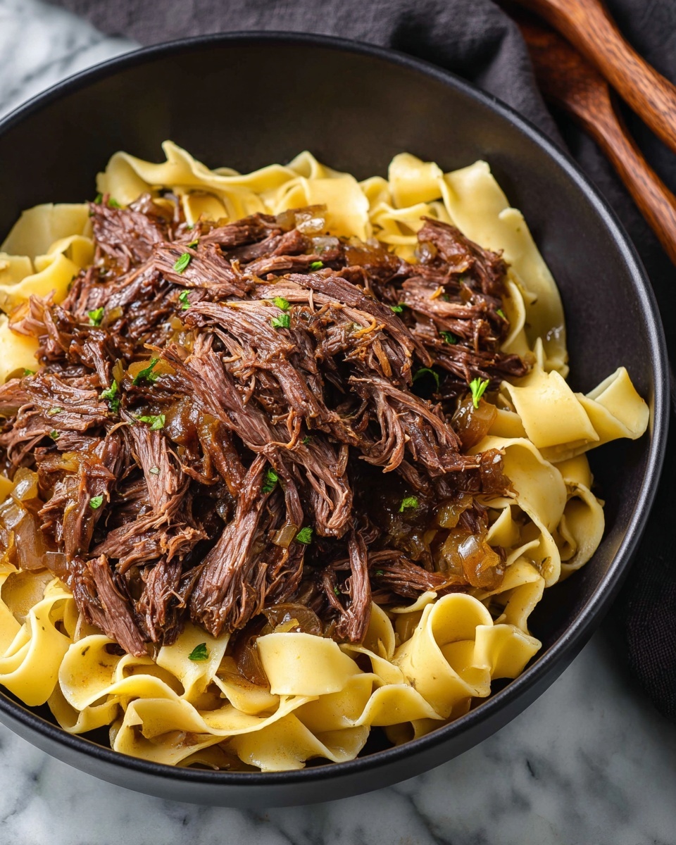 A black bowl holds a bed of light yellow wide noodles at the bottom, layered with a large portion of shredded dark brown beef on top. The beef looks tender and juicy with some small bits of cooked onion mixed in, and there are small green herb pieces sprinkled lightly over the beef and noodles. The background shows a white marbled surface with a dark cloth and wooden utensils partly visible. photo taken with an iphone --ar 4:5 --v 7