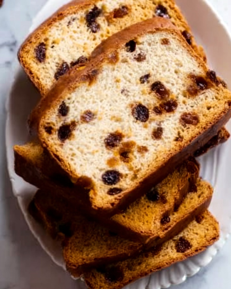 The image shows several thick slices of bread with a golden-brown crust and soft inside, filled with dark spots that look like raisins or chocolate chips. The slices are stacked closely on a white plate with a small scalloped edge, placed on a white marbled surface. The bread’s texture looks slightly crunchy on the outside and moist inside. photo taken with an iphone --ar 4:5 --v 7