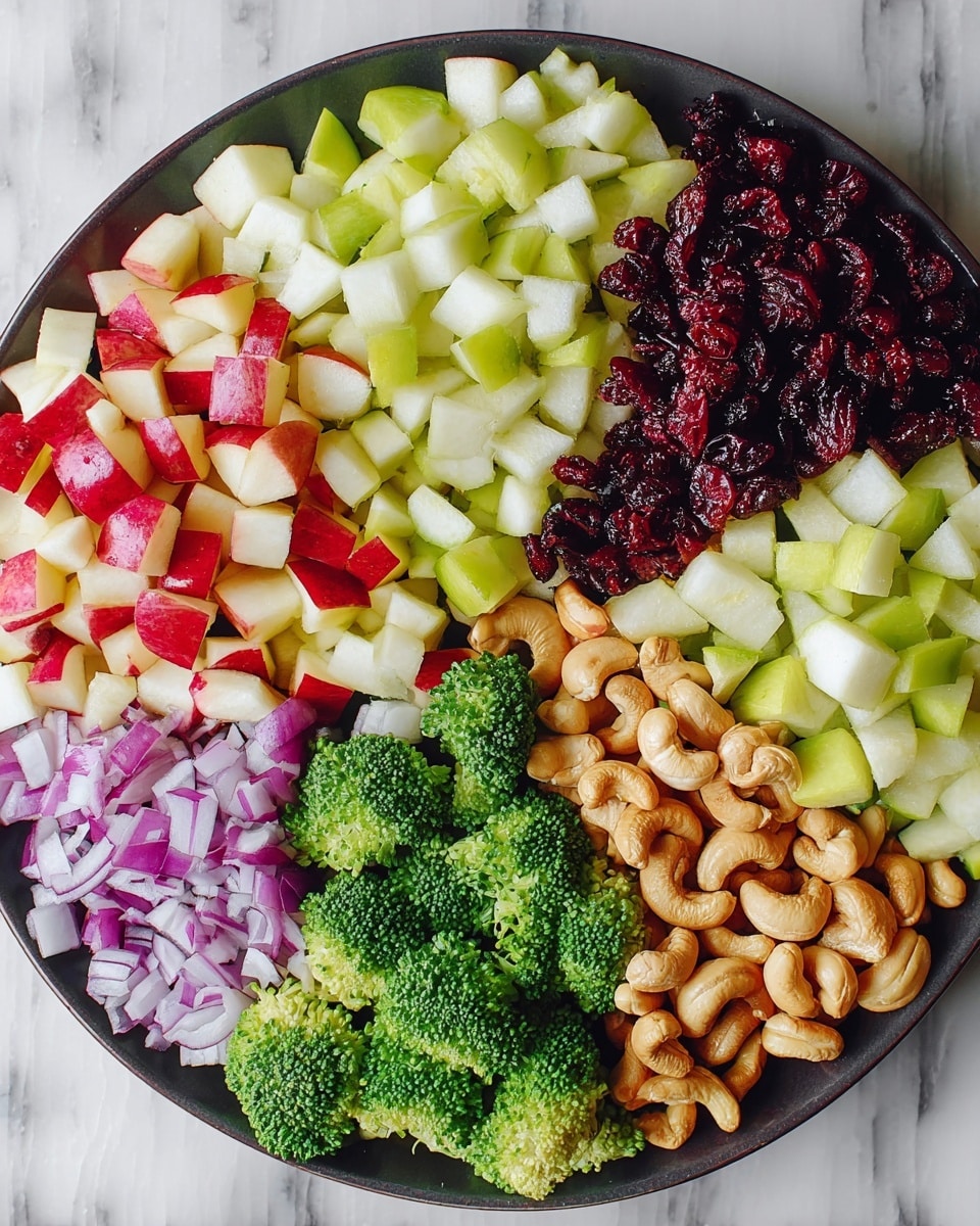 A round white plate holds six distinct layers of ingredients arranged side by side in sections. Starting from the top left and moving right, there is a layer of small red apple pieces with white flesh visible, next to a layer of light green pear chunks that look crisp. Continuing clockwise, there is a section of dark red dried cranberries, followed by a pile of whole, curved cashew nuts colored light brown. At the bottom left, there is a layer of finely chopped purple onion with white highlights, and finally, a section of bright green broccoli florets with a slightly rough texture. The plate is set on a white marbled surface. Photo taken with an iphone --ar 4:5 --v 7