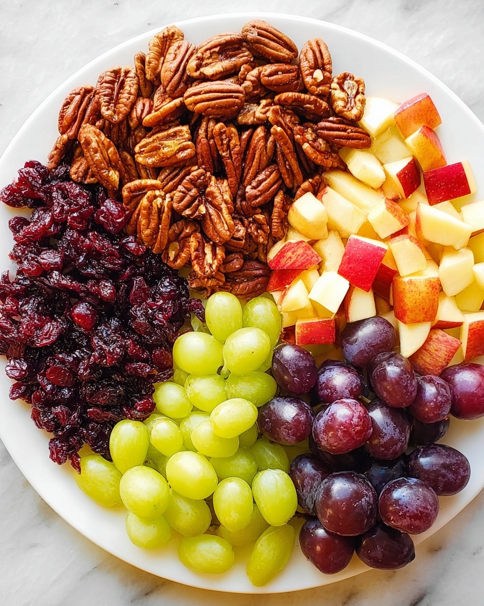 A white plate is divided into five sections, each filled with different food items arranged closely but not mixed. At the top, there is a pile of brown pecan nuts with their rough texture clear. To the right of the pecans are dark red dried cranberries, showing a wrinkled, shiny surface. Below the cranberries is a section of small apple pieces with red skin and pale yellow inside. At the bottom are dark purple grapes with smooth, shiny skins, and to the left of them are light green grapes with a similar smooth and shiny look. The plate sits on a white marbled surface. Photo taken with an iphone --ar 4:5 --v 7