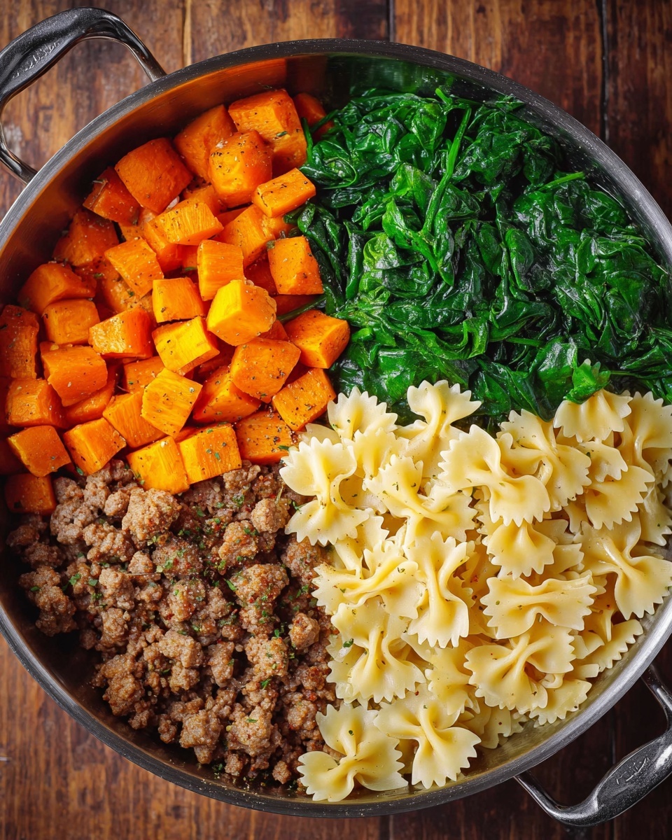 A round metal pan holds a colorful meal divided into four parts: bright orange roasted cubes of sweet potatoes in the top left, vibrant green cooked spinach in the top right, pale yellow farfalle pasta in the bottom right, and browned ground meat in the bottom left with small bits of seasoning mixed in. The pan sits on a brown wooden surface. Photo taken with an iphone --ar 4:5 --v 7