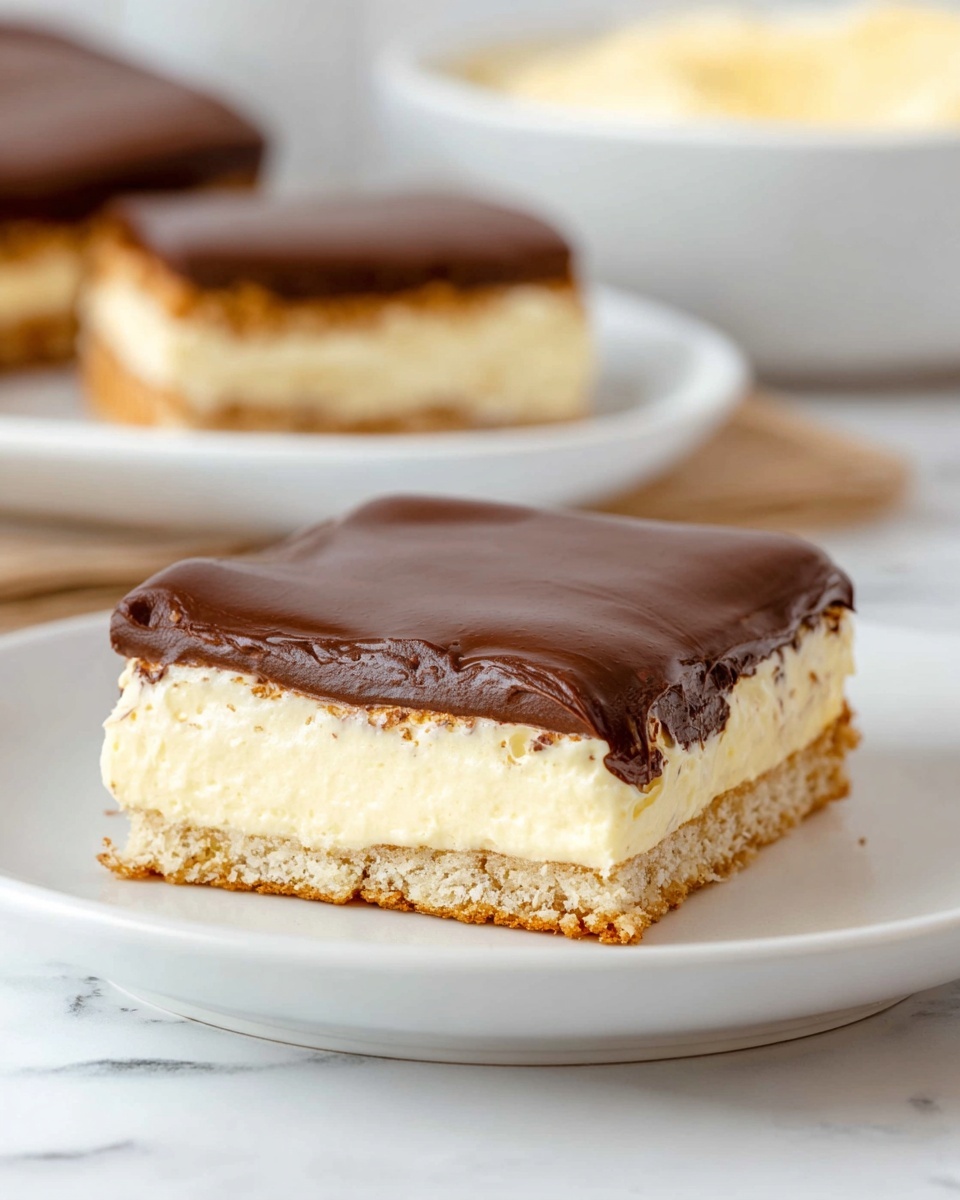 A square dessert piece on a white plate shows three distinct layers. The bottom layer is light brown and crumbly, looking like a biscuit or cake base. The middle layer is thick, creamy, and pale yellow with a soft texture, suggesting a mousse or cream filling. The top layer is a smooth, dark brown chocolate coating that is shiny and evenly spread. The white plate sits on a white marbled surface, with another piece of the same dessert blurred in the background on a similar white plate, and a white bowl with a pale yellow cream visible behind that. Photo taken with an iphone --ar 4:5 --v 7