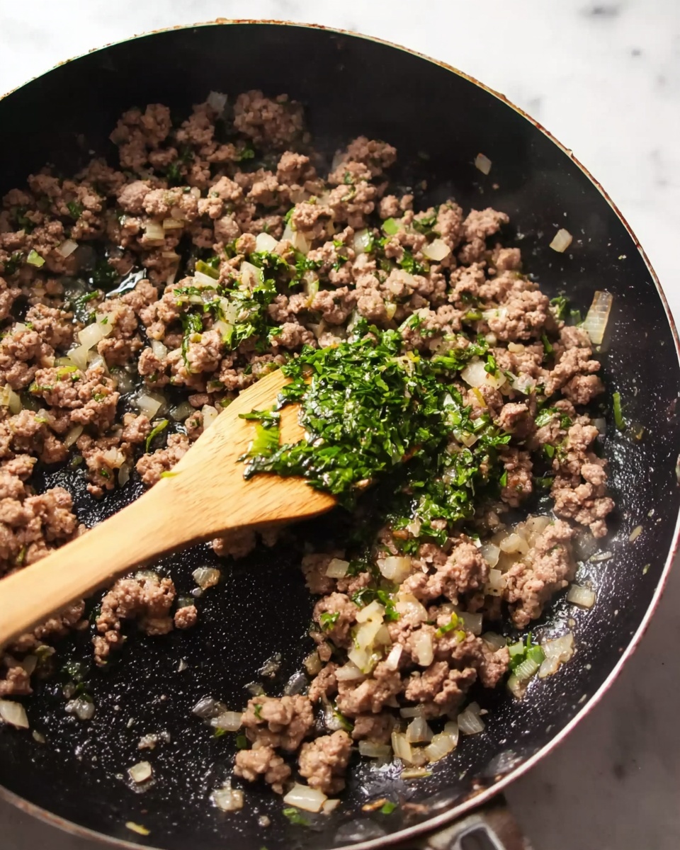 A close-up view of a black frying pan filled with cooked ground meat mixed with small bits of onions and green herbs scattered on top. A wooden spatula with green herb pieces sticks out from the mixture, resting in the center of the pan. The meat is browned and crumbly, with some moisture and oil around the edges. The cooking pan sits on a white marbled surface, catching natural light from the side, showing some steam rising gently from the hot food photo taken with an iphone --ar 4:5 --v 7