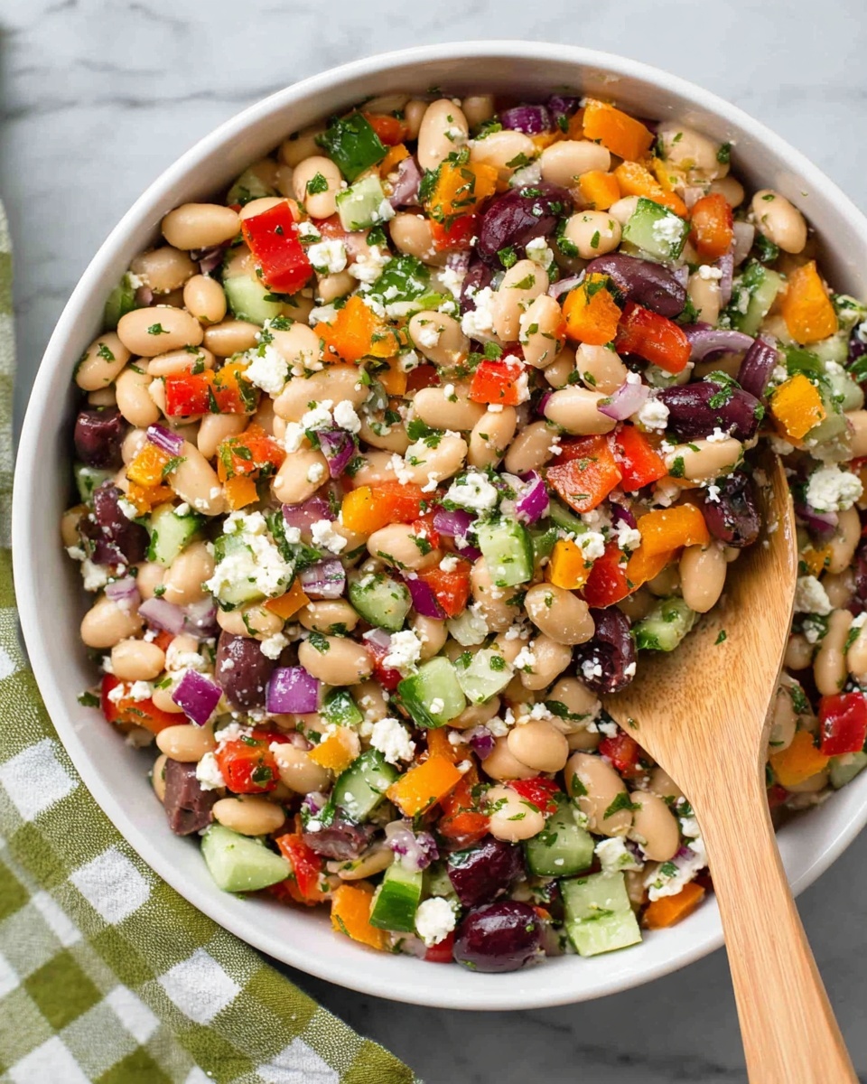 A white bowl filled with a colorful bean salad showing three main layers: a base of small white beans, mixed with black olives and chickpeas; the middle layer has diced red, orange, and yellow bell peppers with finely chopped cucumbers and red onions; the top layer is sprinkled with crumbled white cheese and finely chopped green herbs, sitting on a white marbled surface with a white cloth with green lines under the bowl and a wooden spoon beside it, photo taken with an iphone --ar 4:5 --v 7