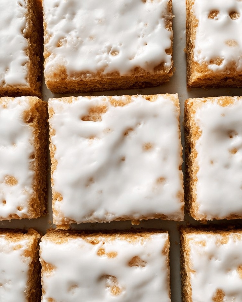 The image shows a close-up view of nine square pieces of baked dessert arranged in a 3x3 grid. Each piece has a light golden-brown base layer that looks crumbly and textured, topped with a smooth white icing layer that covers most of the surface but with uneven edges and some spots where the base is visible. The squares have clean-cut edges and sit closely together, showing thin gaps between them. The overall look is soft and slightly rough from the base texture, with a glossy, smooth top layer. The photo taken with an iphone --ar 4:5 --v 7