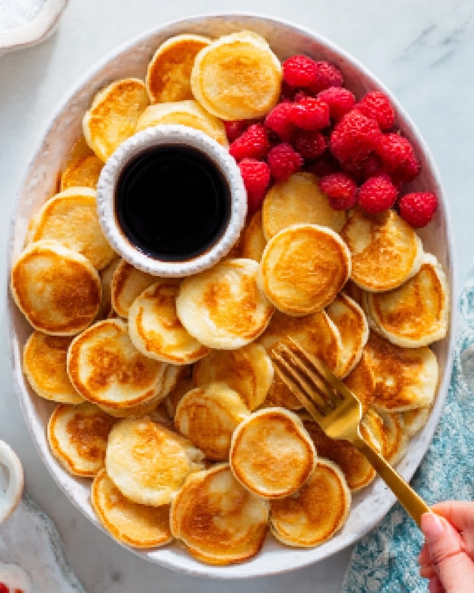 A white plate on a white marbled surface holds many small, round pancakes stacked together, each pancake golden brown with soft, textured edges. On the right side of the plate, there is a cluster of fresh, red raspberries adding a pop of color. A black metal cup filled with dark syrup is in the center of the plate. A woman's hand is holding one of the mini pancakes, dipping it into the syrup. The lighting is bright, emphasizing the warm colors and textures of the pancakes and the shiny surface of the syrup. photo taken with an iphone --ar 4:5 --v 7