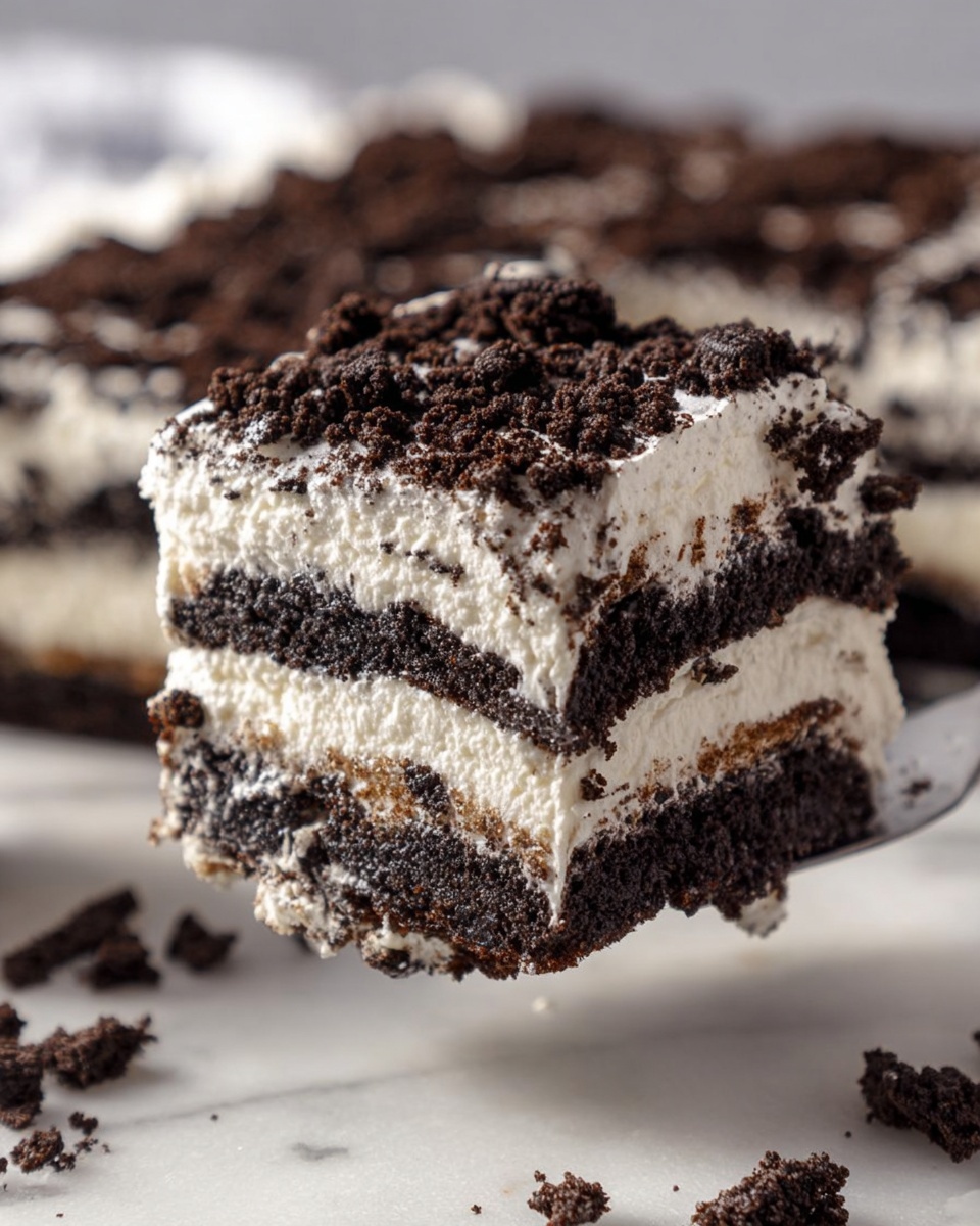 A white square dish holds a layered dessert with four visible layers, alternating between dark brown cookie crumbs and thick white cream. The top layer is completely covered with rough chunks of dark brown cookie pieces scattered unevenly. The side of the dessert shows the distinct layers, making the contrast between the creamy white and dark cookie layers clear. In the background, a white bowl filled with whole cookies and two cookies lying next to it are placed on a white marbled surface. The scene is bright and clean, with crumbs visible on the top edges of the dish. Photo taken with an iphone --ar 4:5 --v 7