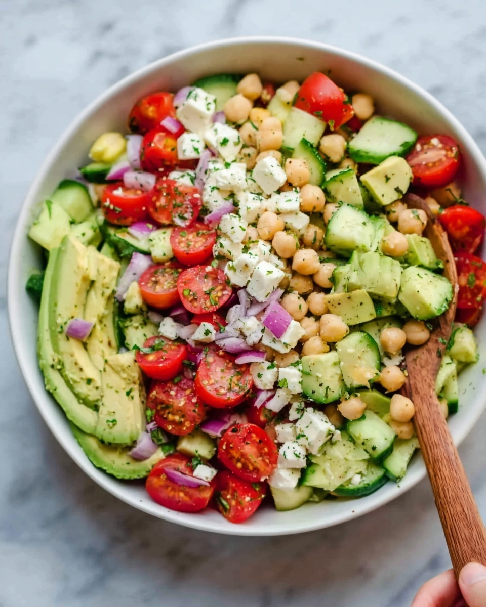 The image shows a colorful salad with several layers of fresh ingredients on a white plate. The base layer has light green cucumber slices with a smooth texture, mixed with beige chickpeas that are round and firm. On top, there are bright red cherry tomato halves with juicy, slightly shiny centers. Small pieces of white cheese with a crumbly texture are scattered throughout. Thin slices of purple-red onion add a crisp contrast. Fresh green cilantro leaves are spread over the salad, adding a leafy texture and bright color. The dish is lightly sprinkled with black pepper. The background is a white marbled surface. Photo taken with an iphone --ar 4:5 --v 7