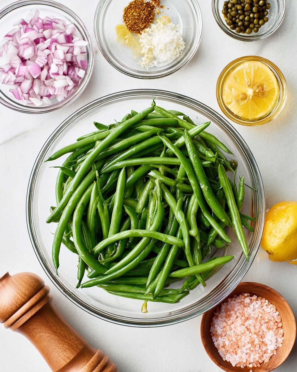 A clear glass bowl in the center is filled with fresh, bright green beans, showing their smooth texture and natural shine. Surrounding the bowl are small clear glass bowls holding finely chopped red onions, whole grain mustard, minced garlic, and chopped capers, each adding a different texture and color: the onions are pale purple and white, the mustard has yellow and brown seeds visible, the garlic is creamy white and soft, and the capers are dark green and slightly wet. To the right is a half lemon with a bright yellow color and a clear glass jar filled with golden olive oil. Below on a white marbled surface is a wooden pepper grinder and a small wooden bowl filled with pink salt crystals. The bright and clean setup highlights the fresh and colorful ingredients used for the recipe preparation photo taken with an iphone --ar 4:5 --v 7