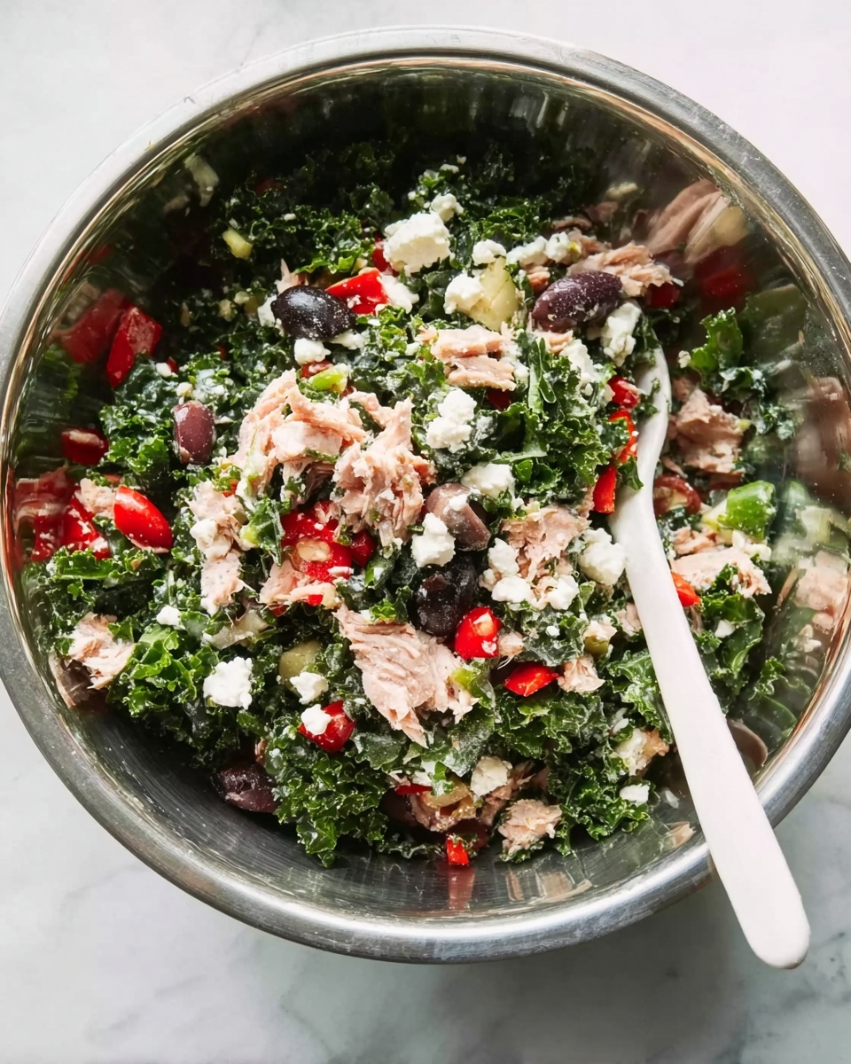 A shiny metal bowl filled with a fresh salad consisting of roughly chopped dark green kale as the base layer mixed with small pieces of red bell pepper, black olives, and small chunks of pink tuna on top. Scattered white creamy chunks of cheese are spread through the salad, adding a soft texture contrast. A white spoon rests inside the bowl on the right side, with a white marbled surface underneath, giving a clean and fresh look. Photo taken with an iphone --ar 4:5 --v 7