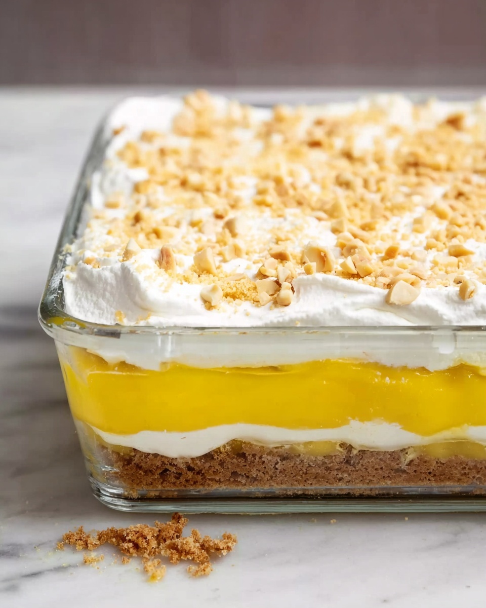 The dish shows a clear rectangular glass container with three visible layers, placed on a white marbled surface. The bottom layer looks crumbly and brown, resembling crushed nuts or cookies. On top of this is a thick, smooth, bright yellow layer that appears like a creamy pudding. The top layer is fluffy and white, like whipped cream, and is sprinkled with small light brown nut pieces. The edges show a bit of crumb falling out from the container. Photo taken with an iphone --ar 4:5 --v 7