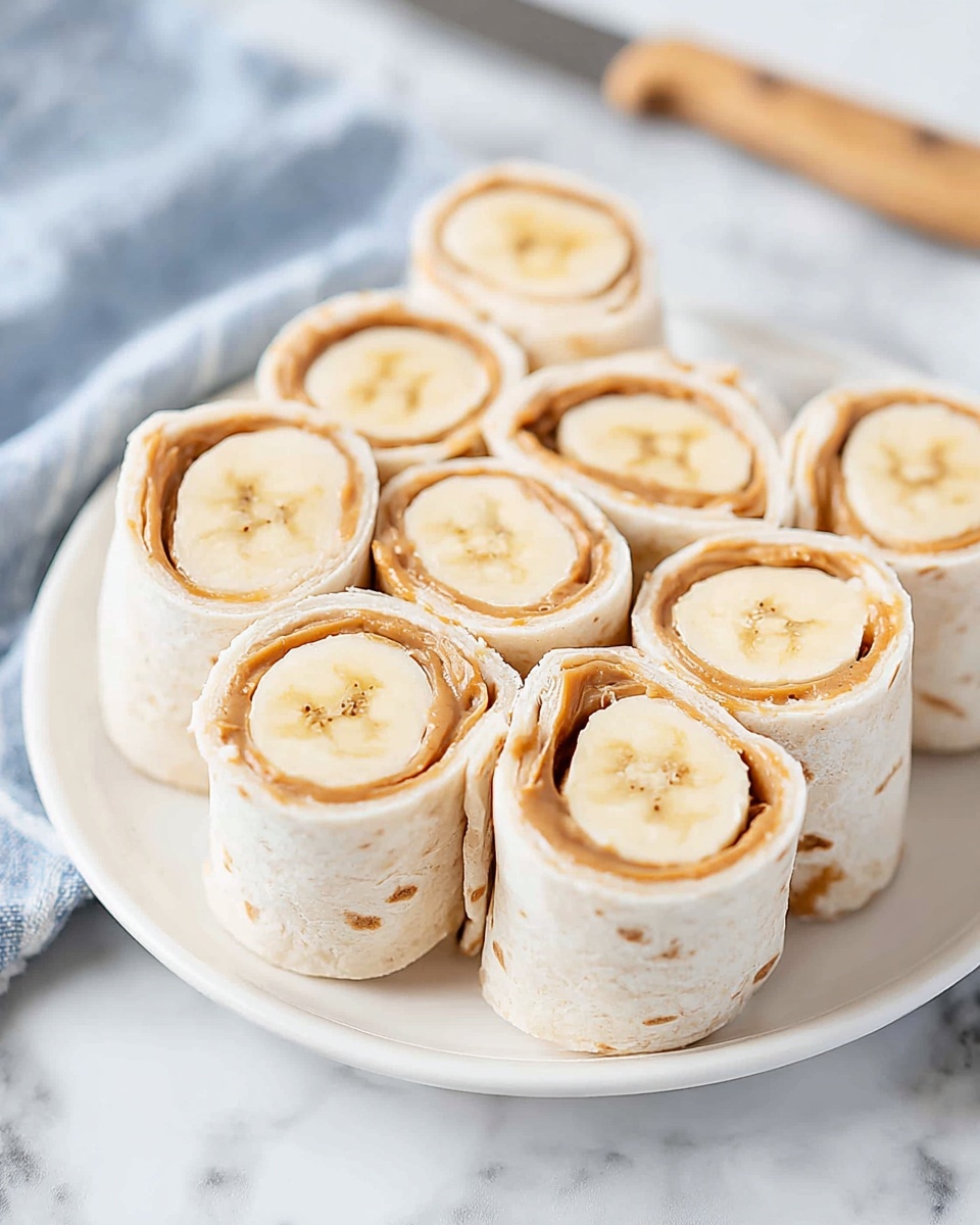 Six banana and peanut butter wraps are arranged tightly on a white plate. Each wrap has three visible layers: the outer white soft tortilla, a middle creamy light brown peanut butter layer, and a central thick banana piece with pale yellow color and slight star-shaped inner detail. The plate sits on a white marbled surface with a blurred knife and blue cloth in the background. Photo taken with an iphone --ar 4:5 --v 7