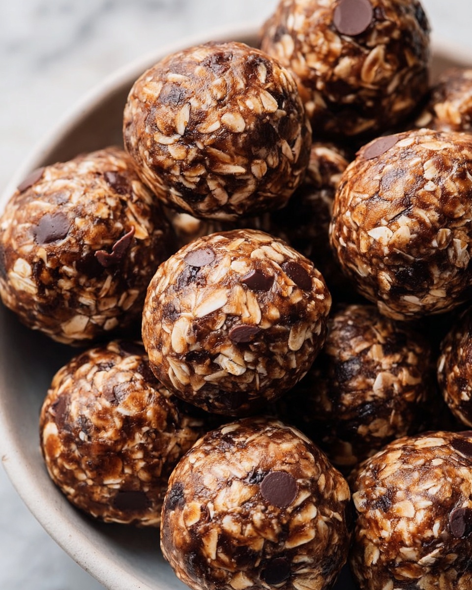The image shows round chocolate oat energy balls closely packed together in a white bowl on a white marbled surface. Each ball has a rough texture with visible oat flakes and dark chocolate chips mixed inside, giving a mix of light beige and rich brown colors. The balls are dense and uniform in size, with some chocolate chips slightly melted into the oat mixture. The overall look is chunky and inviting, with a natural, homemade feel. Photo taken with an iphone --ar 4:5 --v 7