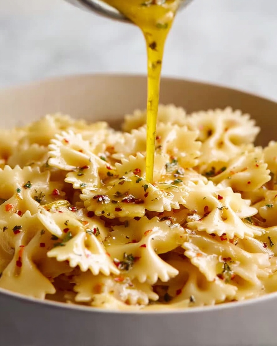 A white bowl filled with cooked bowtie pasta, showing a light beige color with slightly curled edges and textured ridges. A yellow sauce with visible small red and green herbs is pouring from above, slowly coating the pasta from the top center. The scene is set on a white marbled surface, with a blurred background adding depth. The focus is on the pasta and sauce interaction, emphasizing the sauce’s creamy, smooth flow over the textured pasta shapes. Photo taken with an iphone --ar 4:5 --v 7