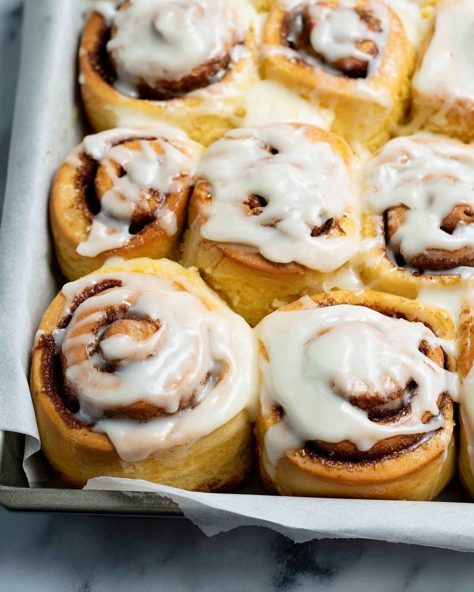 The image shows three cinnamon rolls on a dark blue textured surface, with swirls of golden-brown dough forming the base layer, a second layer of cinnamon filling visible in the spiral pattern, and the top layer covered with a thick spread of white cream cheese frosting that looks smooth and creamy. The rolls appear soft and fluffy with slight shine from the glaze under the frosting and are positioned close to each other with one almost centered in the image. photo taken with an iphone --ar 4:5 --v 7