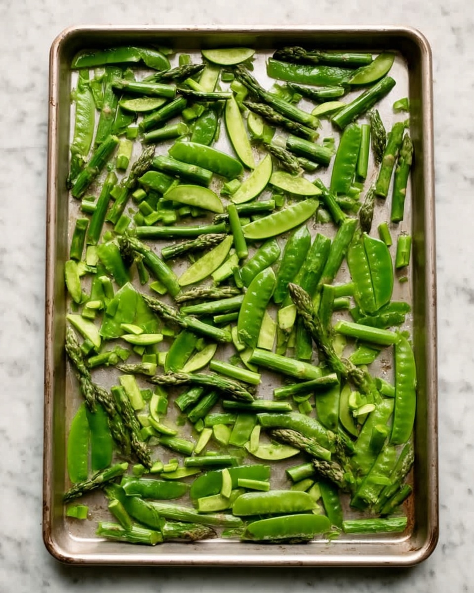 A metal baking tray filled with a single layer of green vegetables spread evenly across its surface. The vegetables include cut asparagus stalks, snap peas, and snap pea pods, all bright green with a fresh, slightly glossy texture. They are arranged loosely, with some pieces whole and others sliced into smaller sections. The tray sits on a white marbled surface. photo taken with an iphone --ar 4:5 --v 7